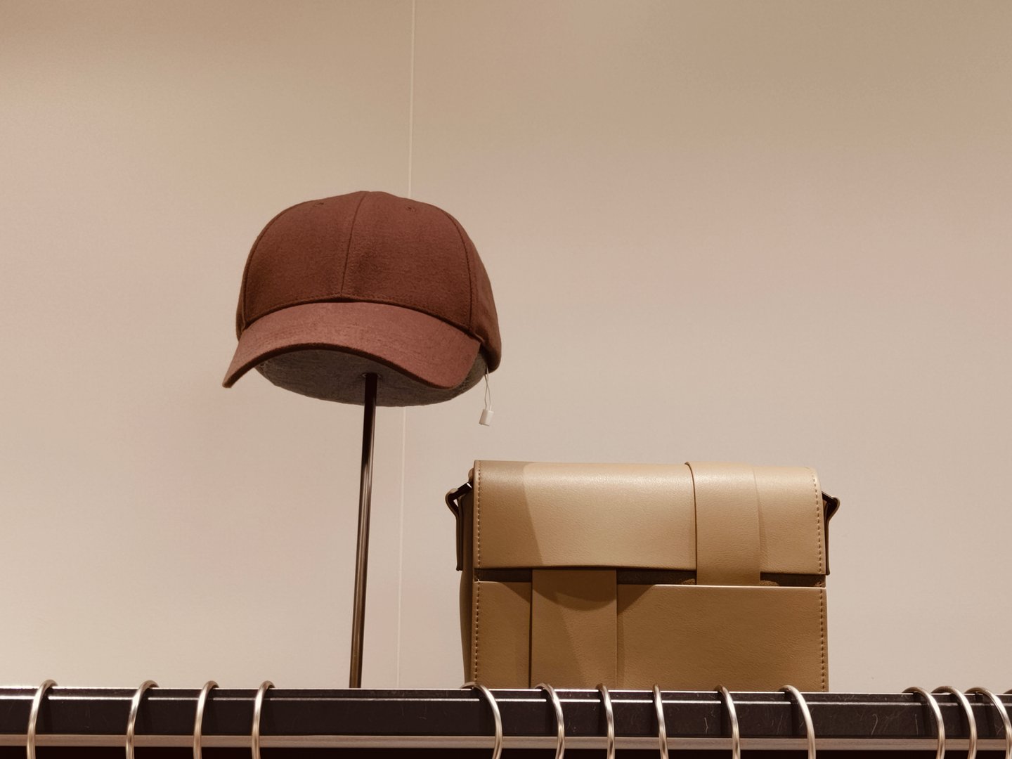 A brown hat and a brown purse are displayed on a shelf. The hat is on a stand and the purse is on a hanger. Concept of style and fashion, with the hat