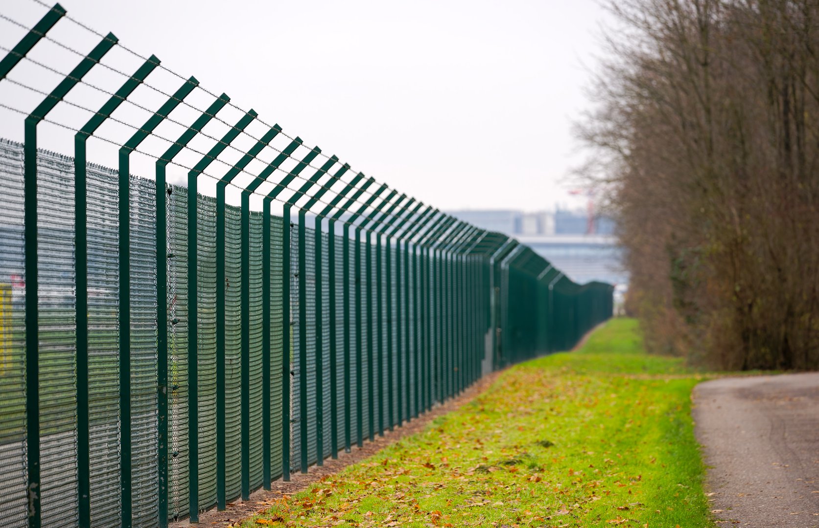 Diminishing perspective of green barbed wire fence at Swiss Airport Zürich Kloten on a gray autumn day. Photo taken November 30th, 2024, Zurich Rümlang, Switzerland.