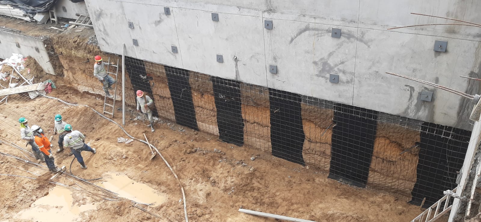 Construction site with workers installing wall reinforcements and insulation on a building foundation.