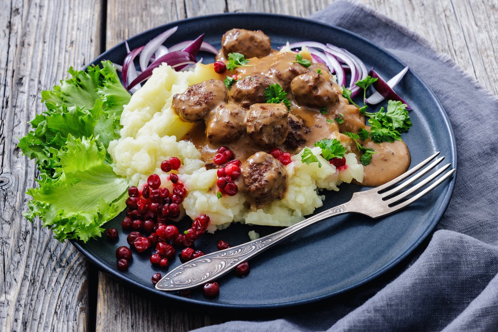 Swedish meatballs with mashed potatoes, creamy gravy, lingonberries and lettuce on a plate