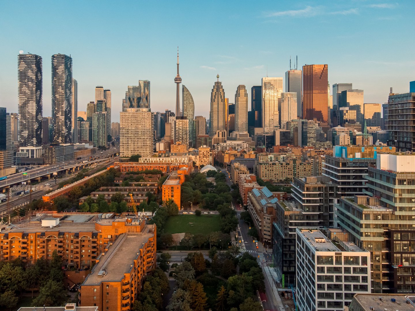 Aerial view of Toronto skyline with iconic CN Tower at sunset, showcasing modern skyscrapers and urban landscape.