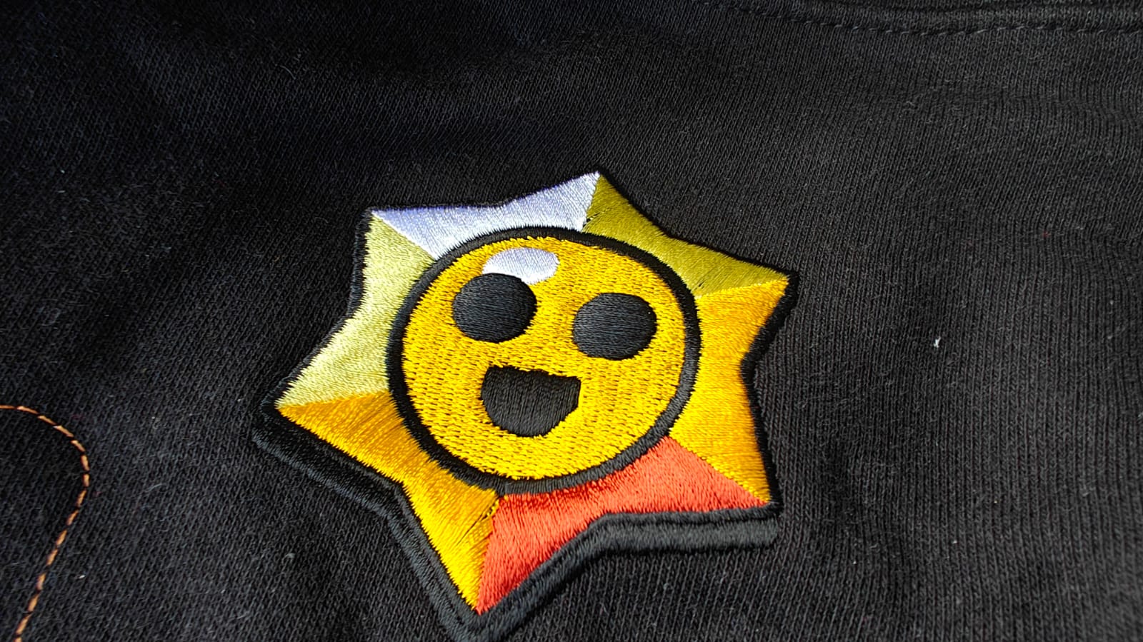 Embroidered star patch with a yellow face and expression on black fabric background.