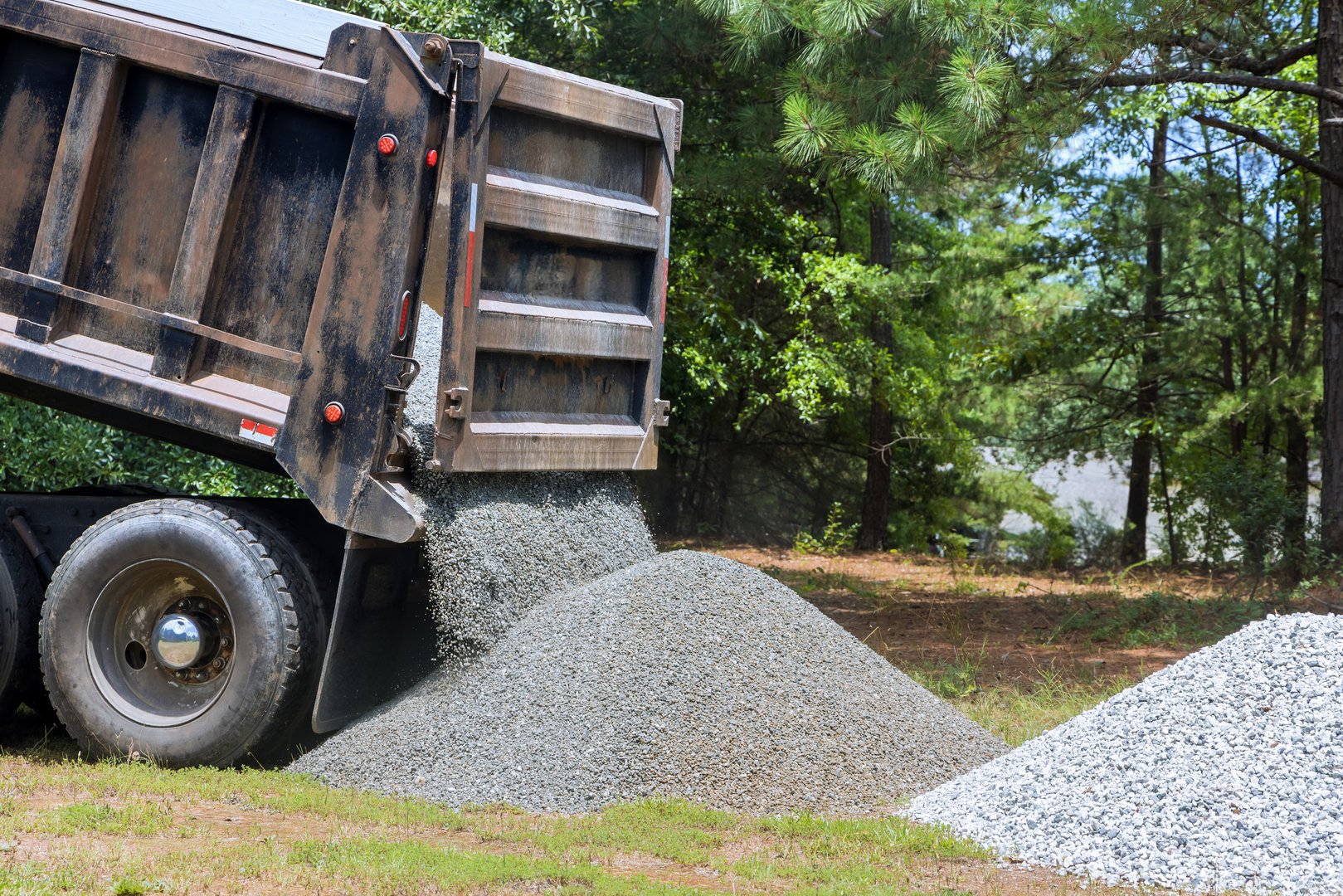 Truck unloads gravel onto grassy area preparing for landscaping work