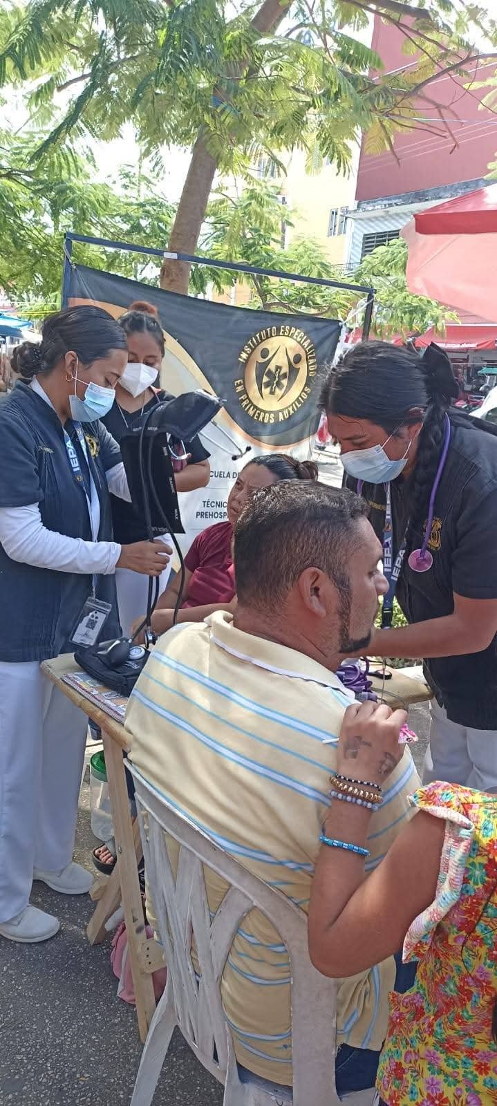 Healthcare workers provide medical check-ups to people seated outdoors under a tent.