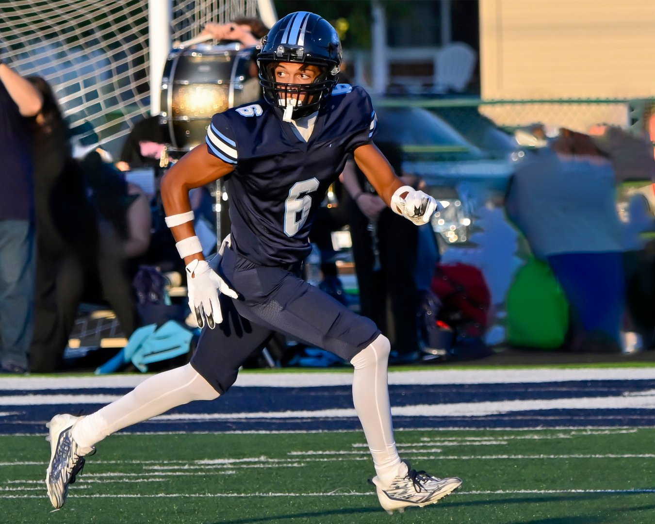 A teenage High school football player beginning to run his route downfield while looking back over his shoulder.