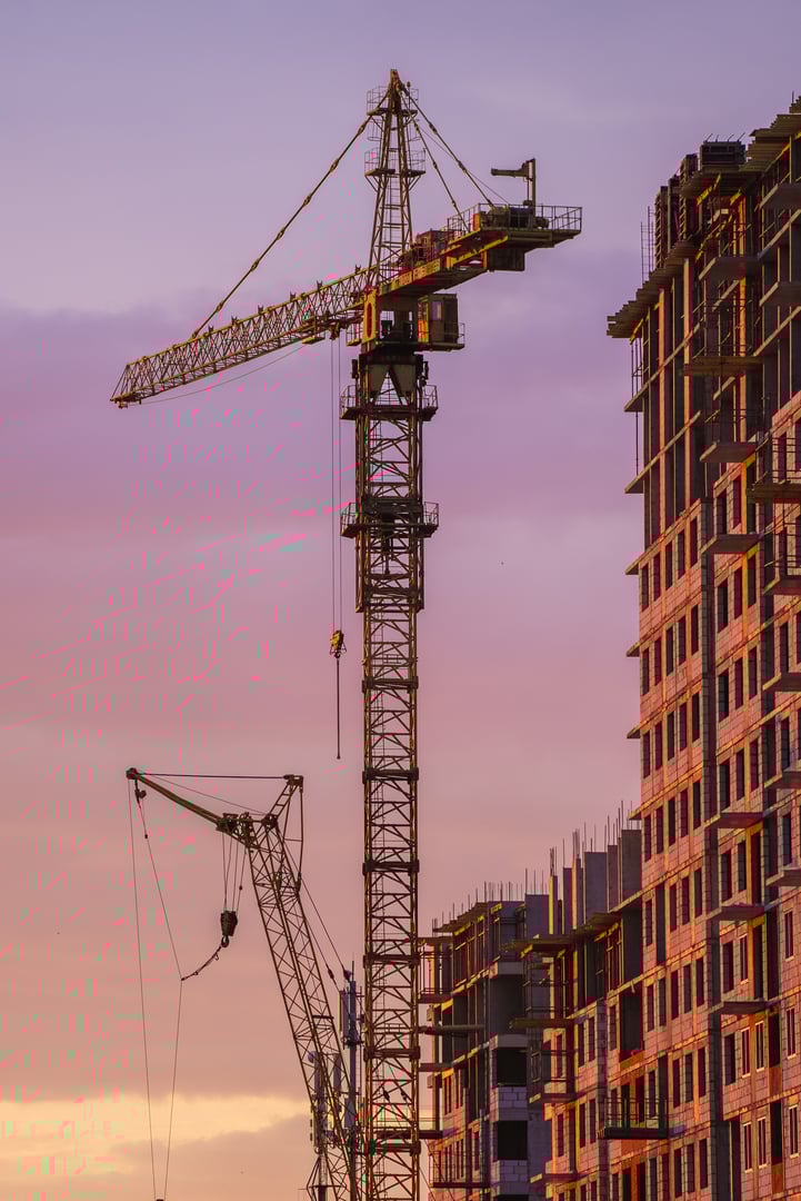Tower cranes are working on constructing a new residential apartment building against a beautiful sunset sky, showcasing urban development and progress