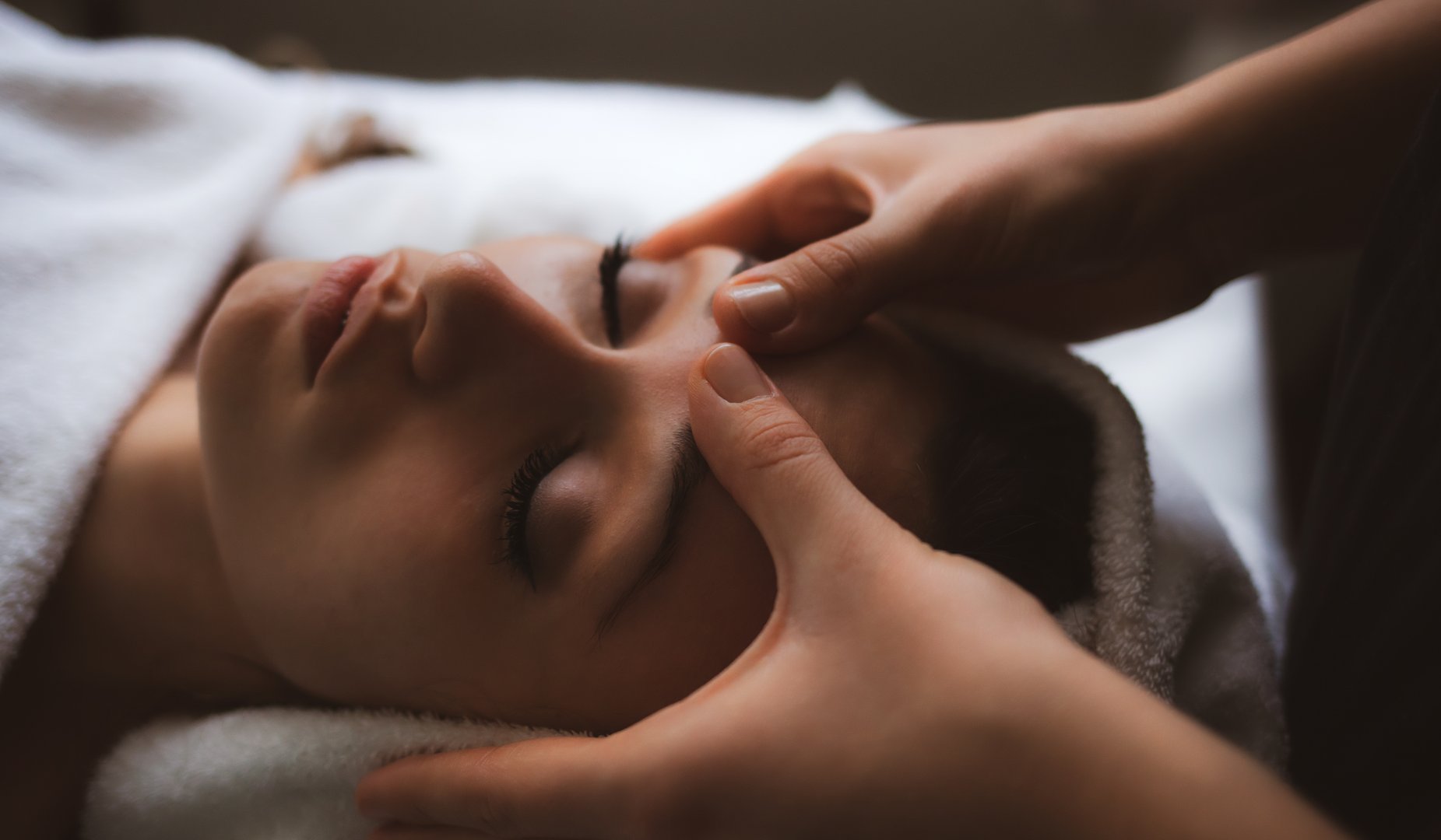 Person receiving a relaxing facial massage, eyes closed, with hands gently pressing on the forehead.