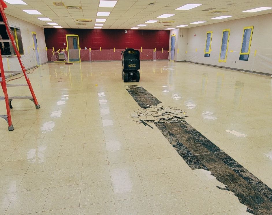 A large indoor space being renovated with a red ladder, exposed flooring, and a floor polishing machine in the center.