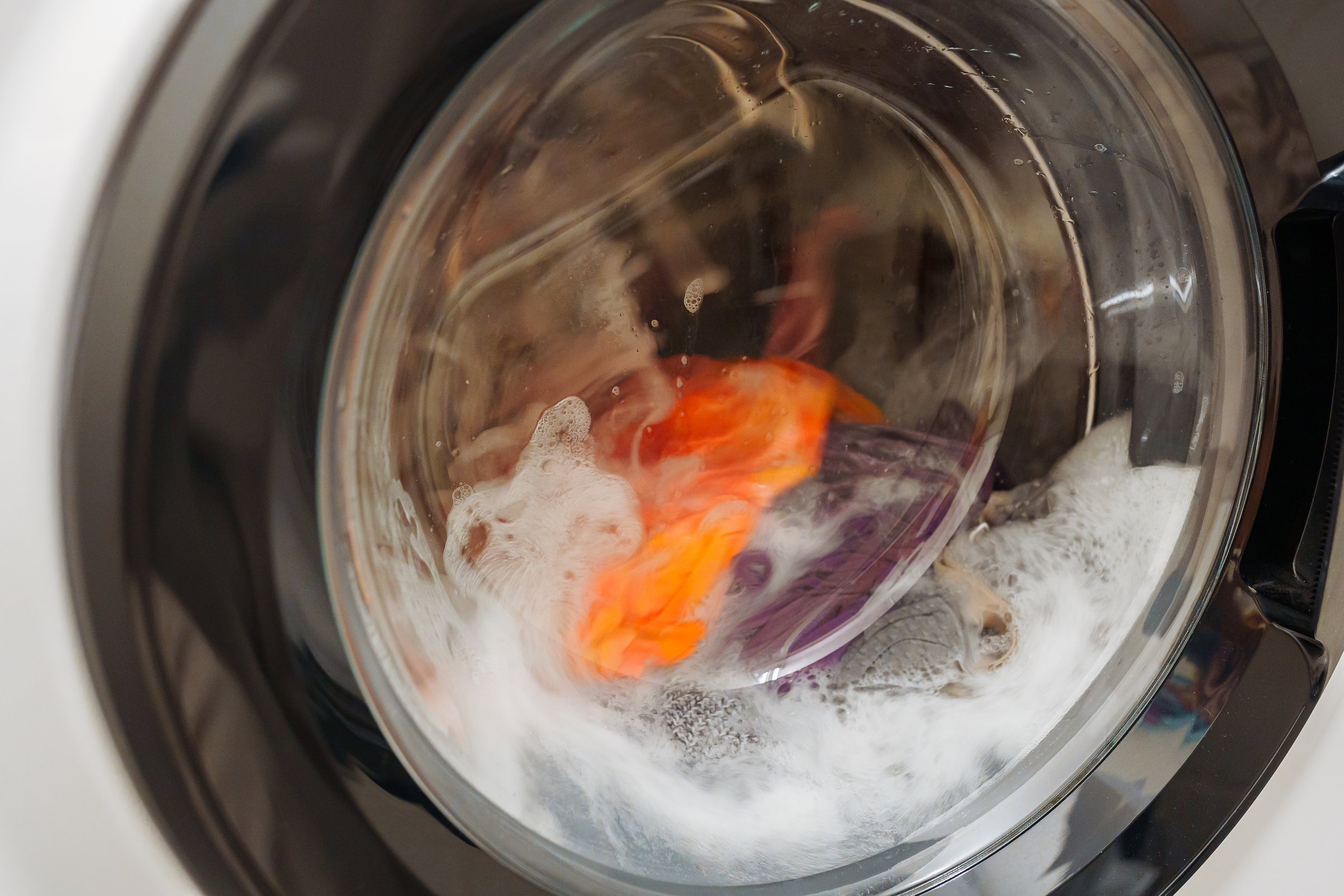spinning drum washing machine with laundry, front loading, modern home appliances, repair. Closeup of washing machine door with spinning laundry