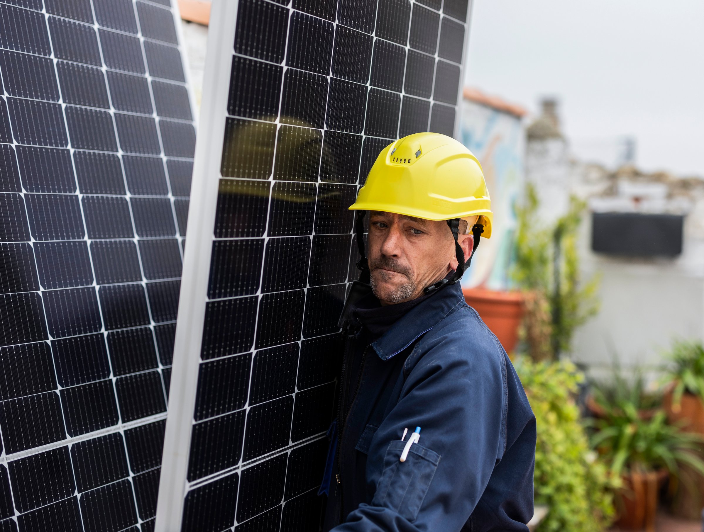 Technician wearing a yellow safety helmet carefully positions solar panels on a rooftop, contributing to sustainable energy solutions and reducing carbon footprint