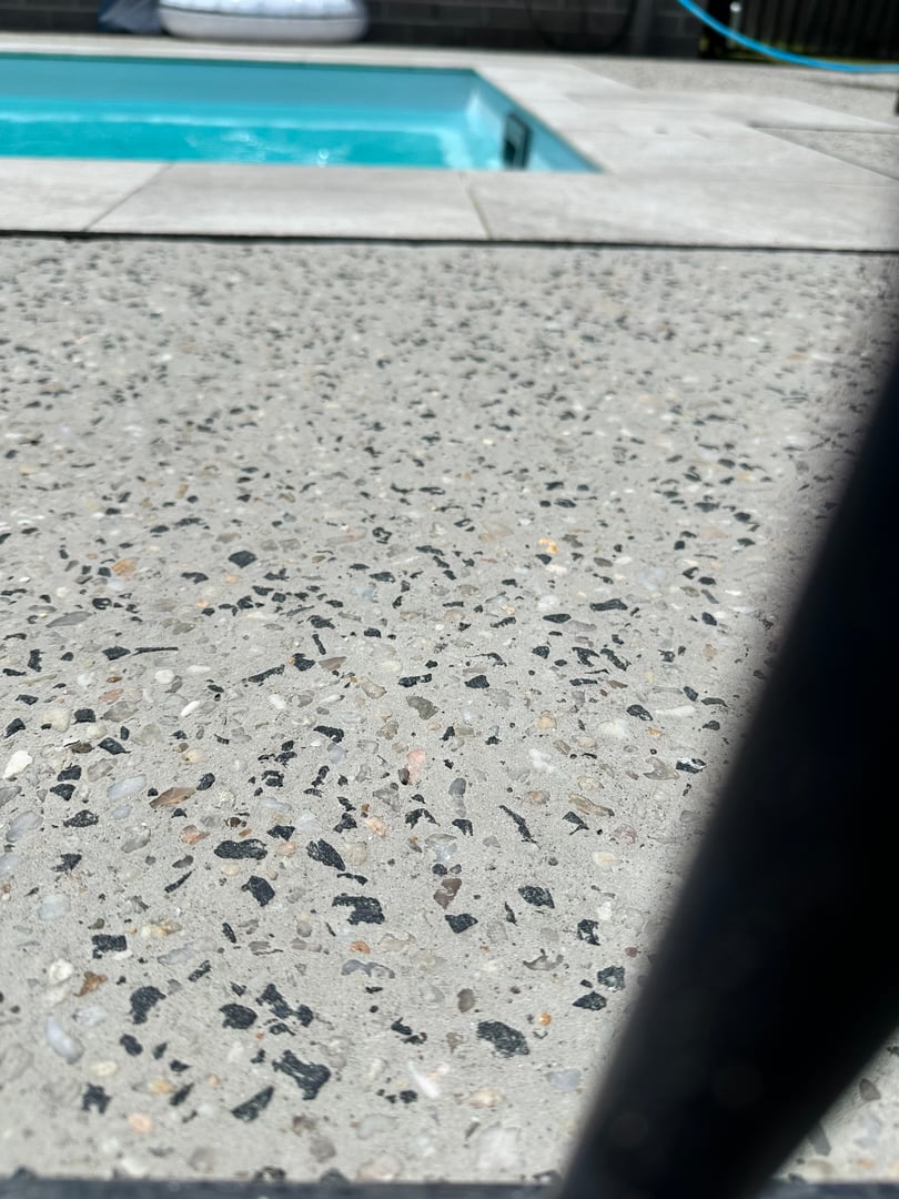 Close-up of a textured concrete surface with a blurry view of a swimming pool in the background.