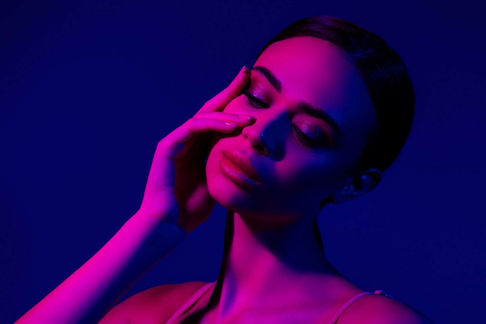 Artistic photography of a young woman illuminated by ultraviolet lighting, emphasizing her beauty. Neon blue and pink tones highlight the contrasts of her features, creating a nightclub-inspired atmosphere.