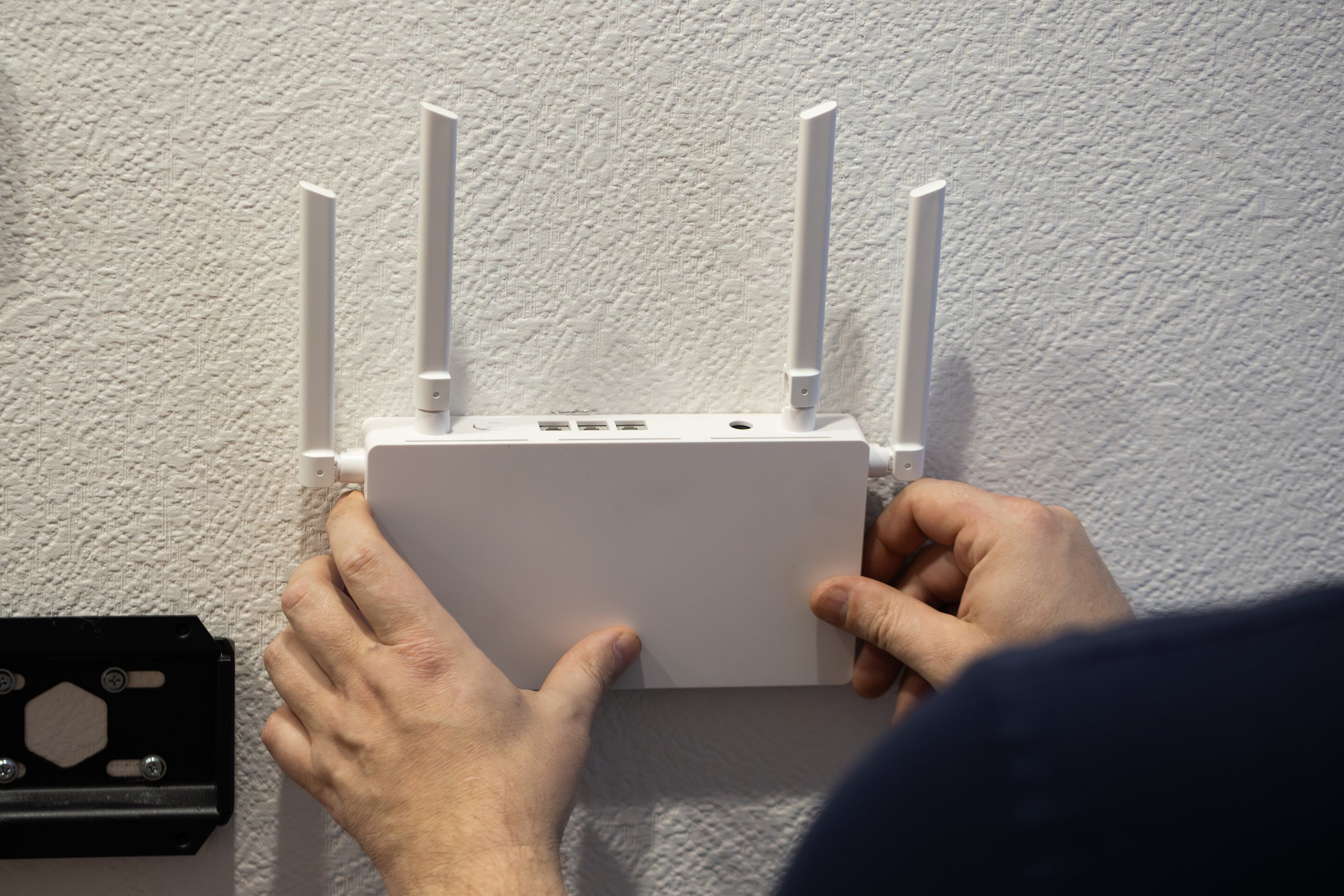 An individual is installing a wireless router with antennas on a wall to improve internet access and connectivity