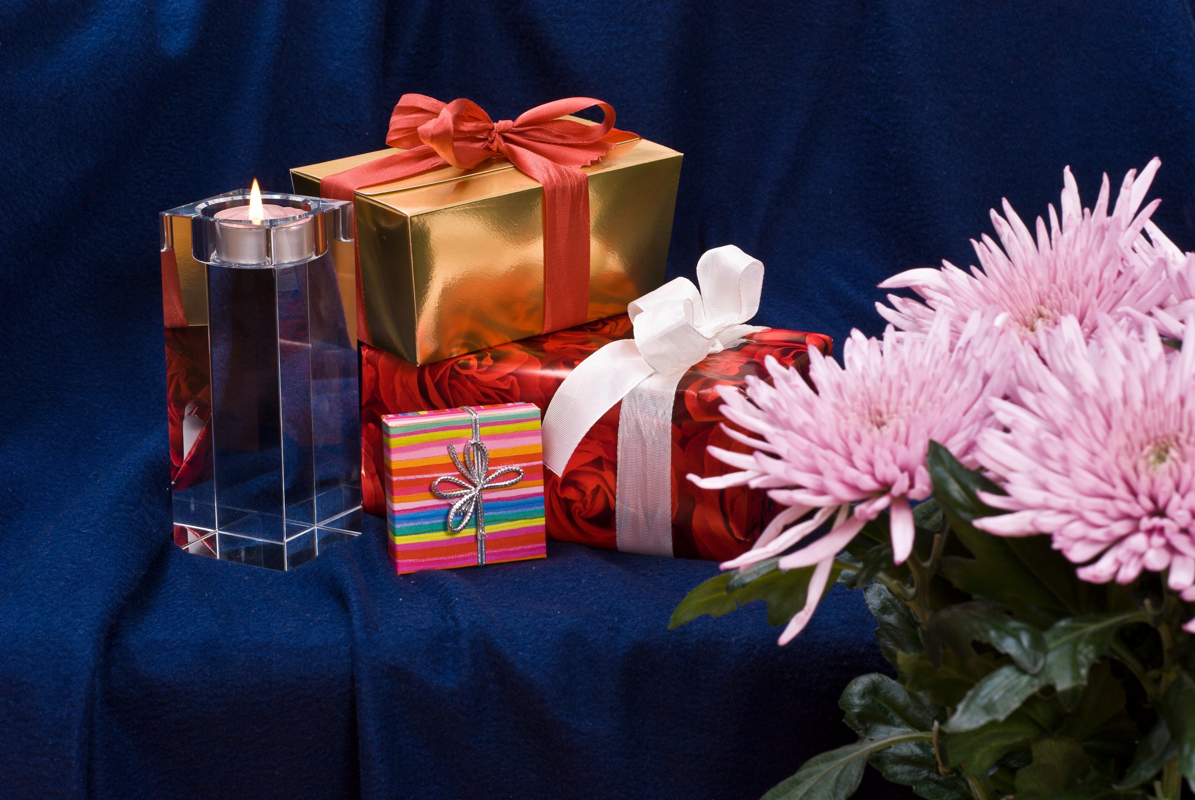 Gifts and burning candle behind flowers. Blue material on the background.