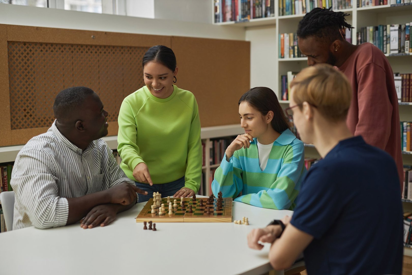Portrait of diverse group of young people in chess class with smiling young woman asking teacher