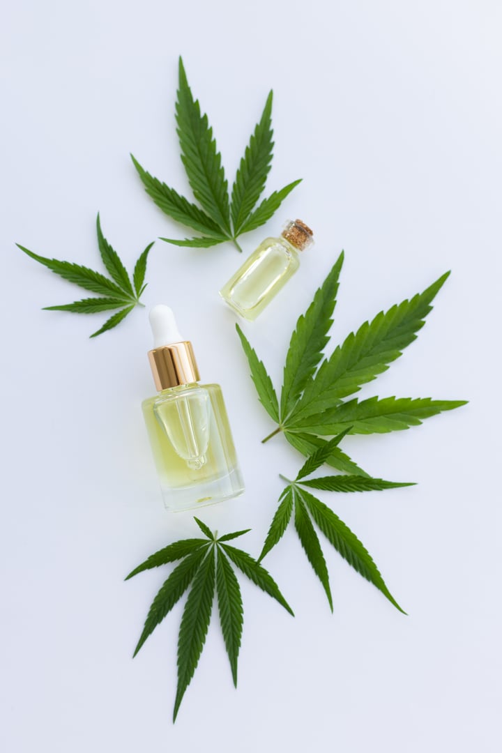 Small bottles with cannabis oil between fresh cannabis leaves. Top view