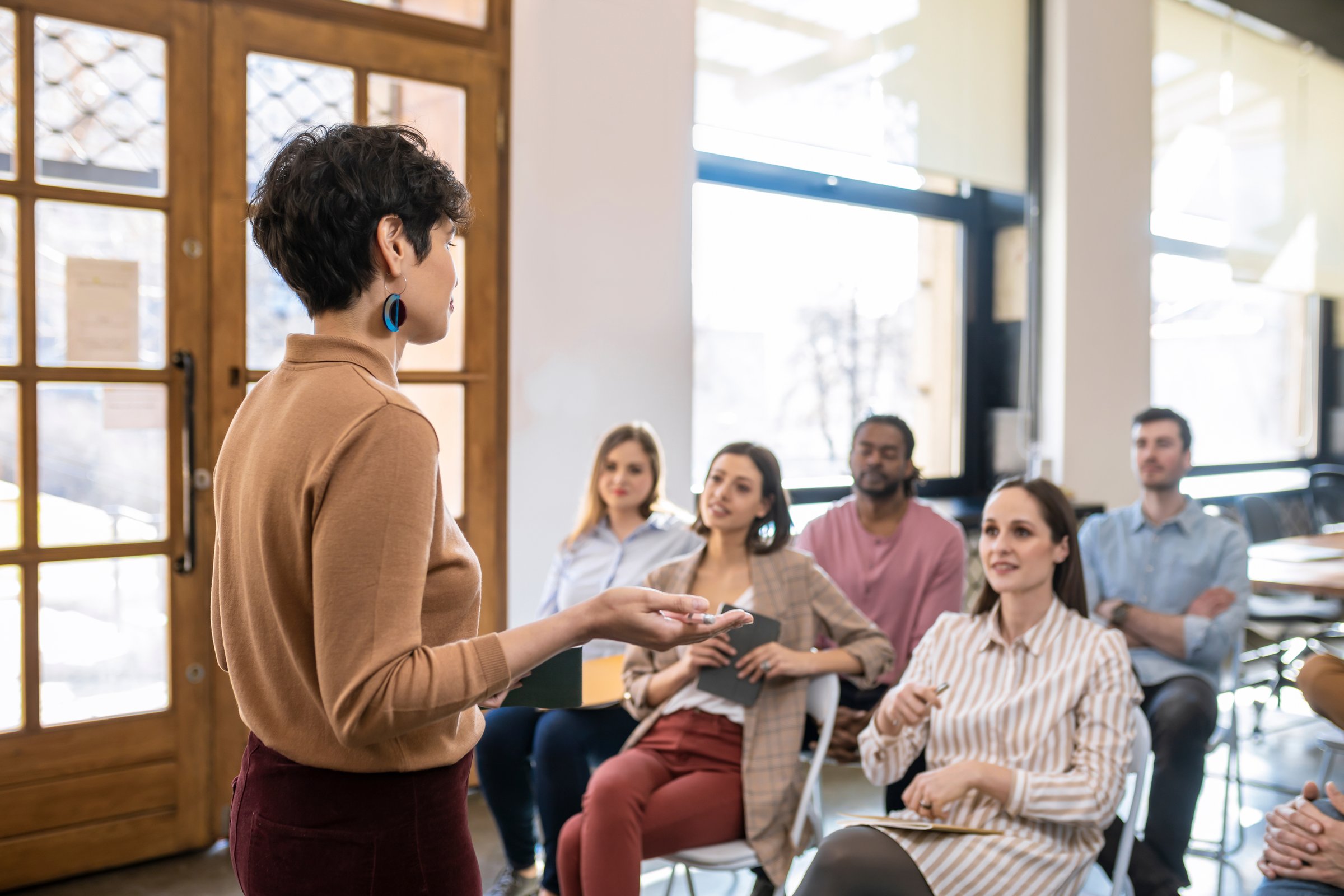 Pretty stylish woman lecturer giving presentation to a group of businesspeople.