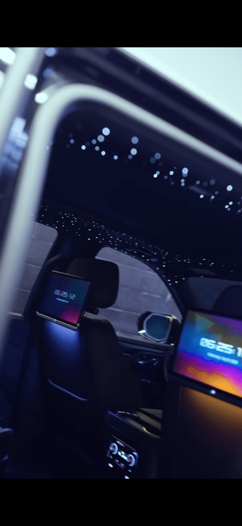 Luxury car interior with starry ceiling, digital screens on headrests, and ambient lighting.