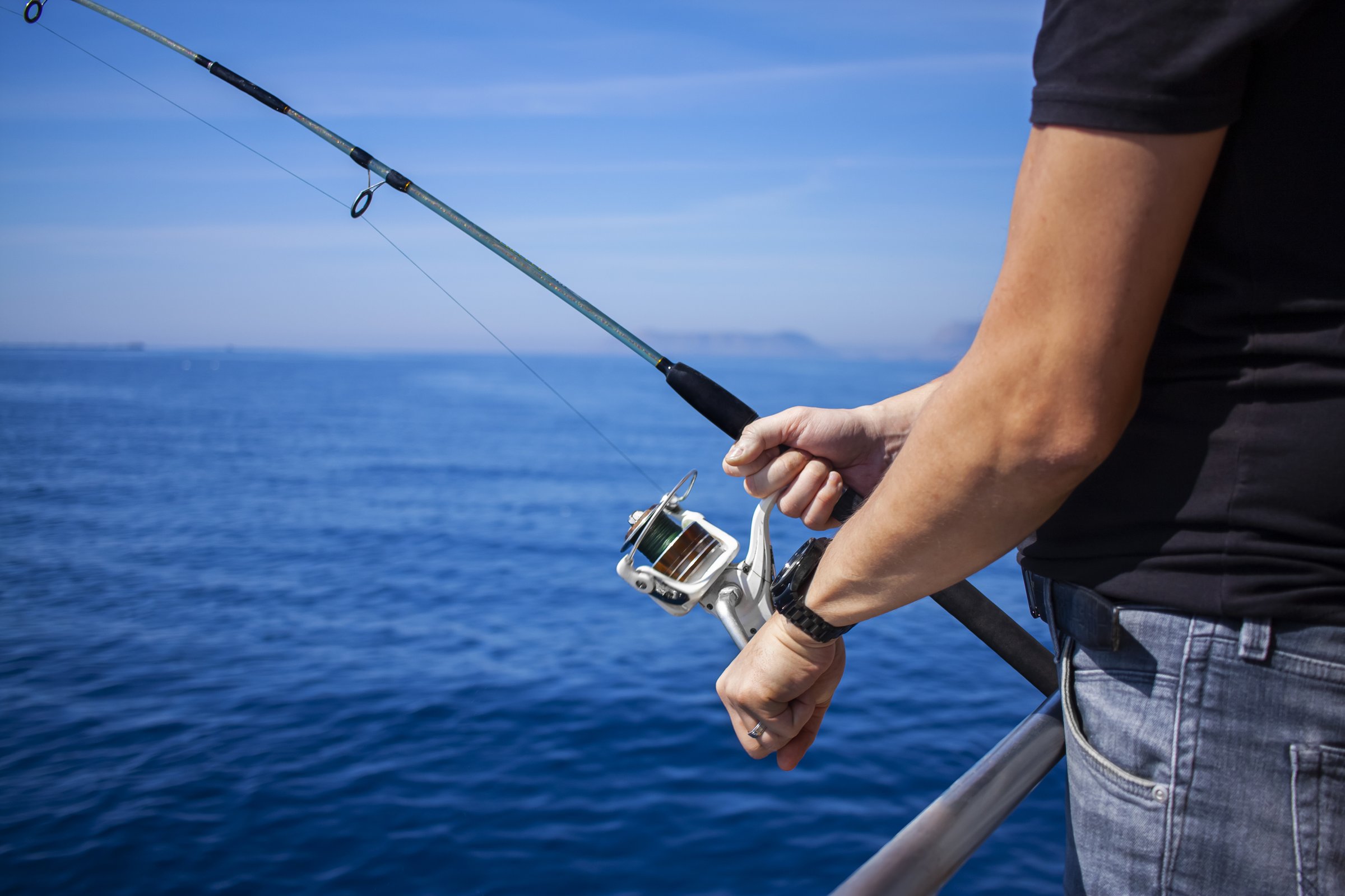 Close-up of man's hand holding fishing rod in the sea, man fishing. Fishing rod with a spinning reel in the hands of a fisherman.