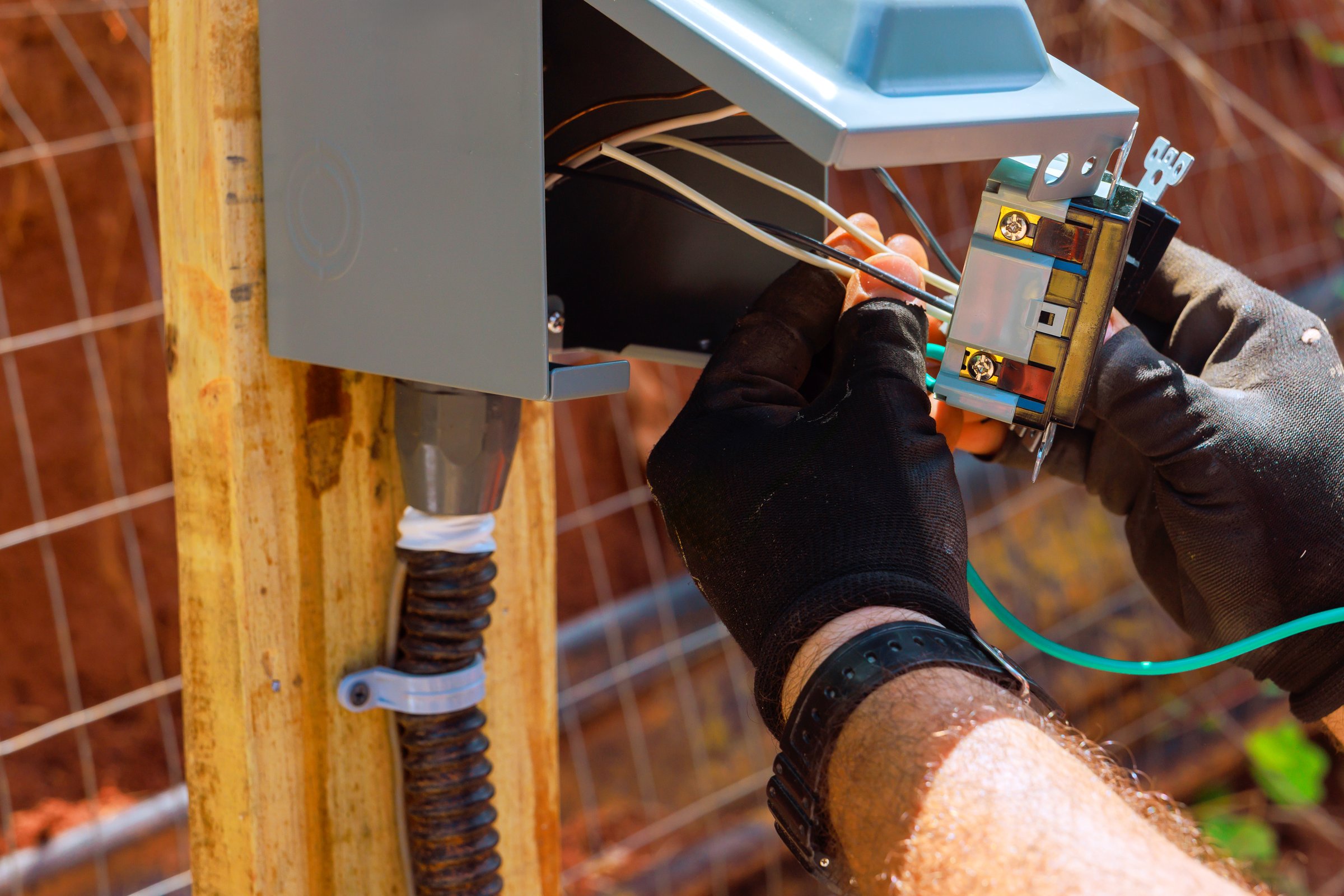 Technician works on outlets connecting wires to an electrical panel mounted outdoors in backyard.