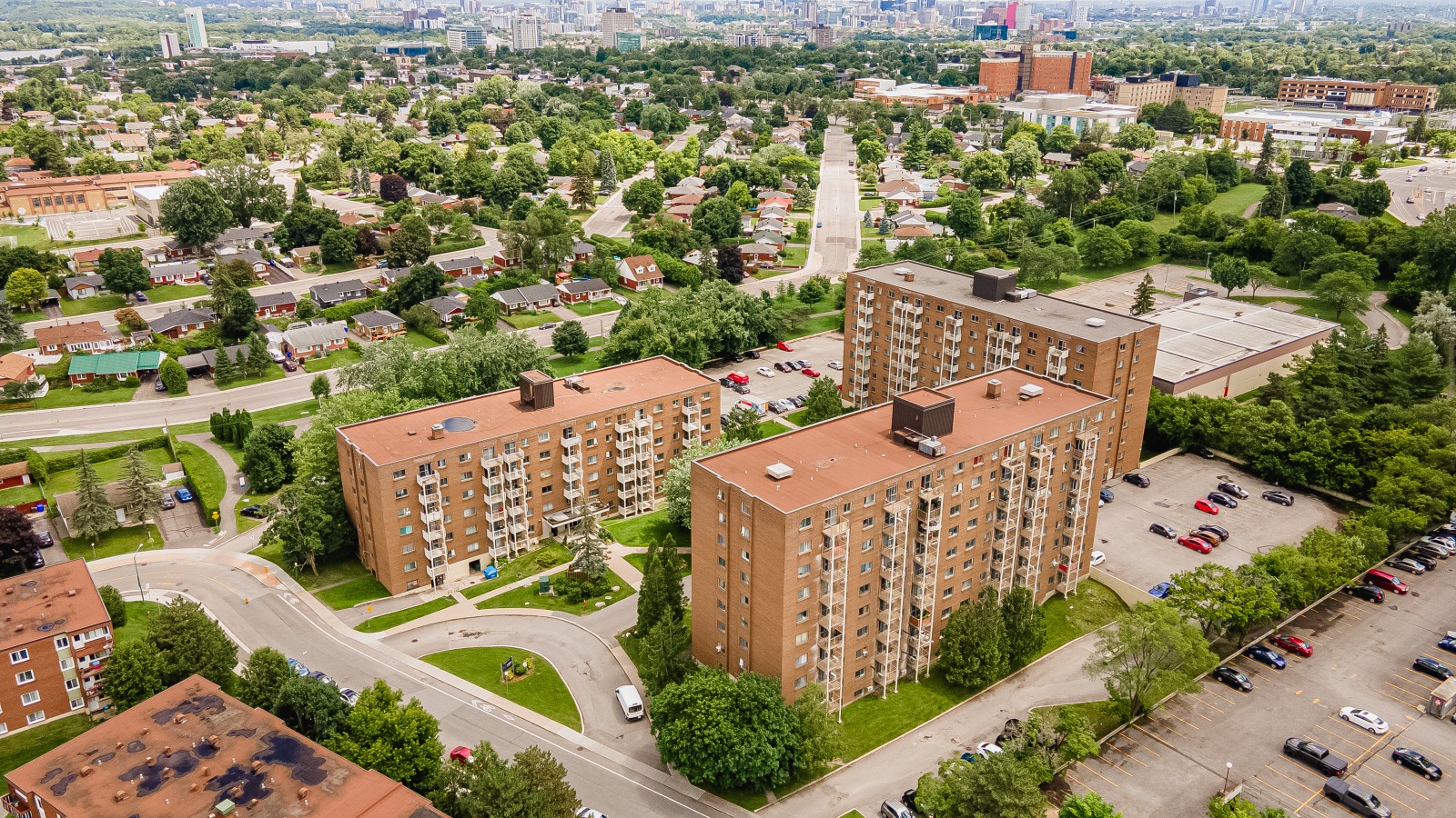 Aerial view of a residential area with three brown apartment buildings surrounded by trees and parking lots.