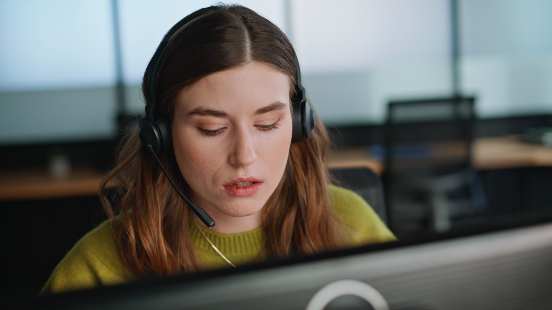 Telemarketing manager consulting in call center closeup. Professional support agent listening customer issue looking monitor. Serious helpdesk assistant woman talking headset in office coworking space