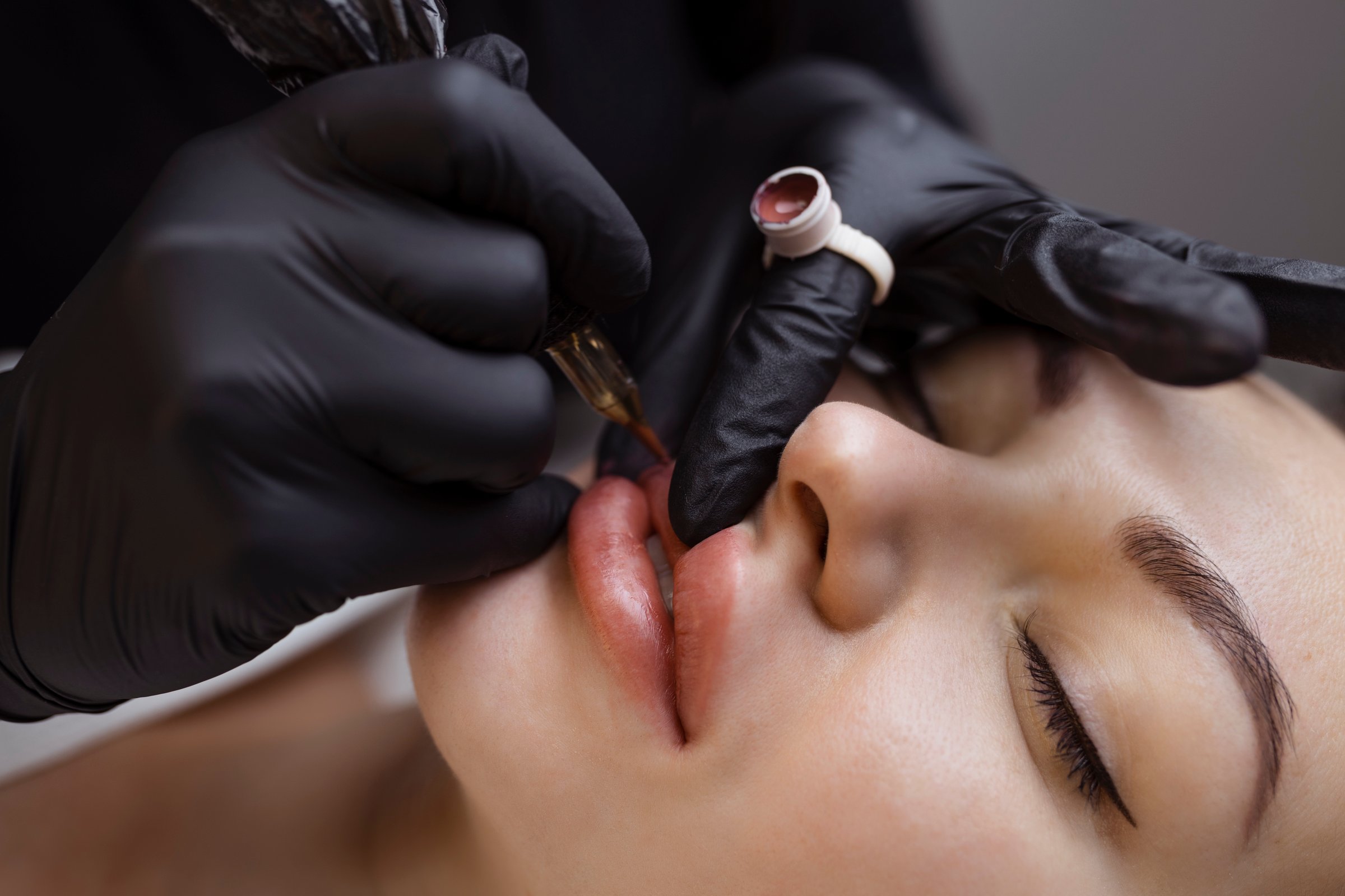 Permanent makeup for nude lips. Cosmetologist in the salon performs a tattoo procedure with a tattoo machine close-up.