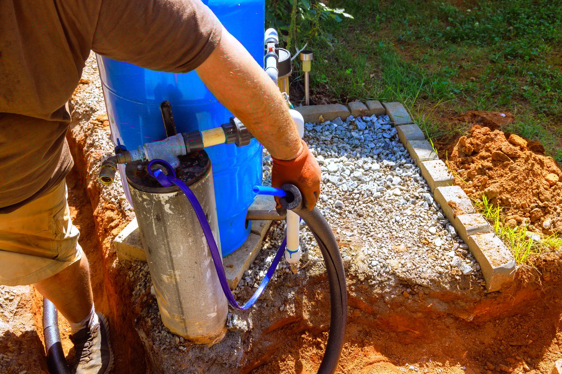 An plumber is connecting artesian water well pump in backyard, home improvement efforts under clear skies.
