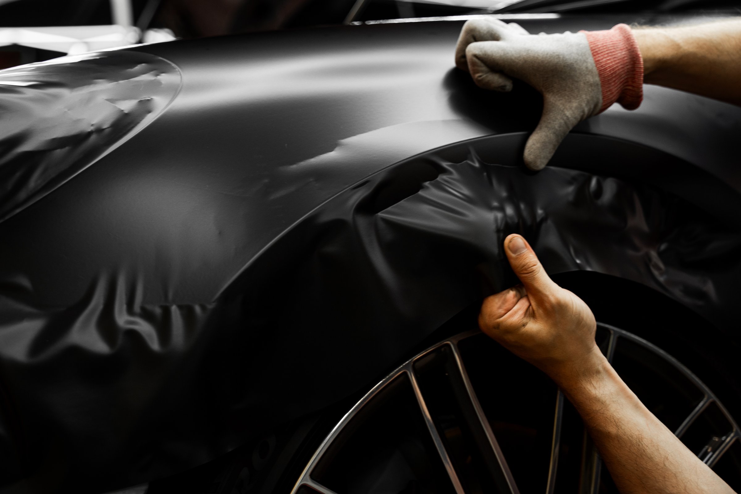 Matte black vinyl wrapping around car with smooth alignment over curves and edges. Matte black vinyl wrap application on front fender and wheel arch of luxury vehicle. Vinyl Wrapping of Car