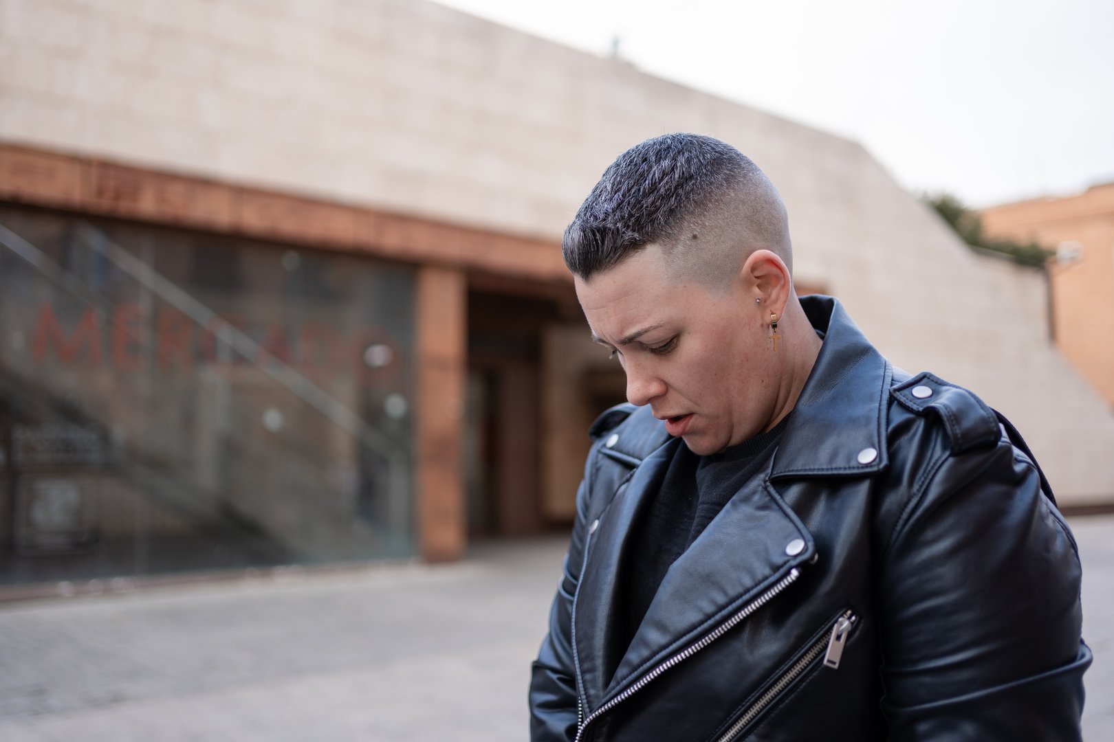 Woman with fade haircut wearing black leather jacket and black t-shirt looking down
