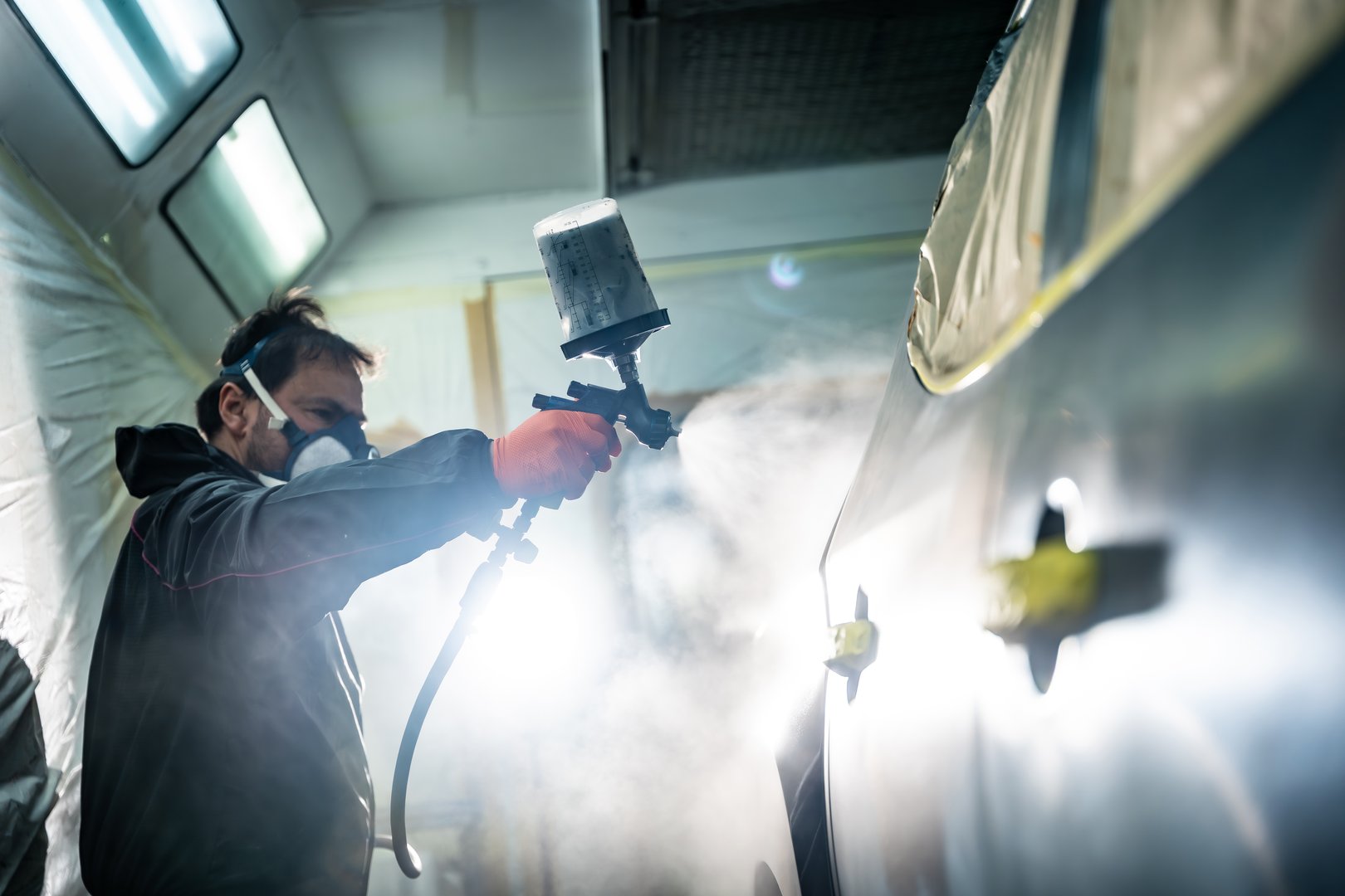 Male auto body painter applying paint to a car door panel
