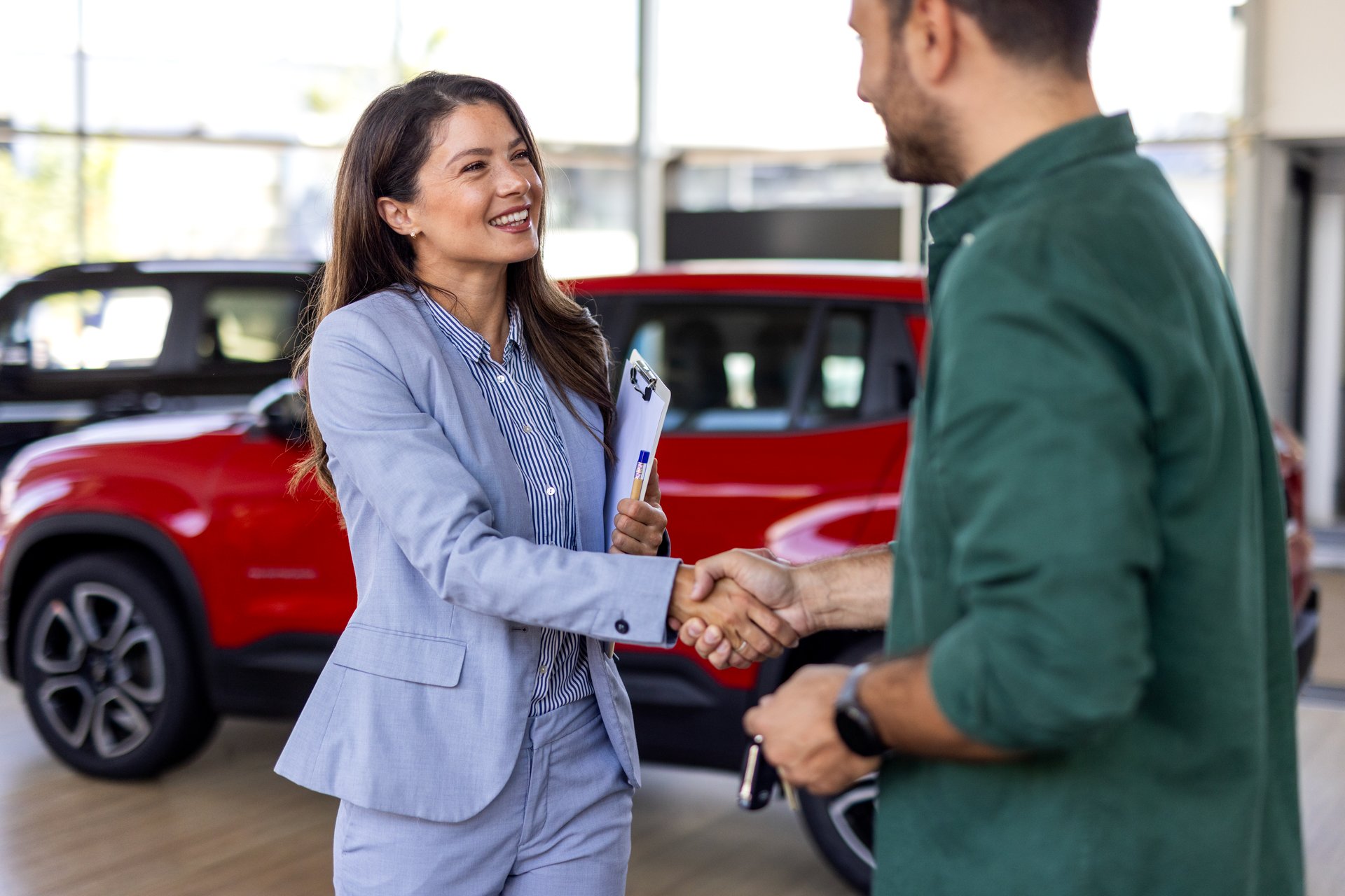 Beautiful young woman is talking to handsome car dealership worker while choosing a car in dealership