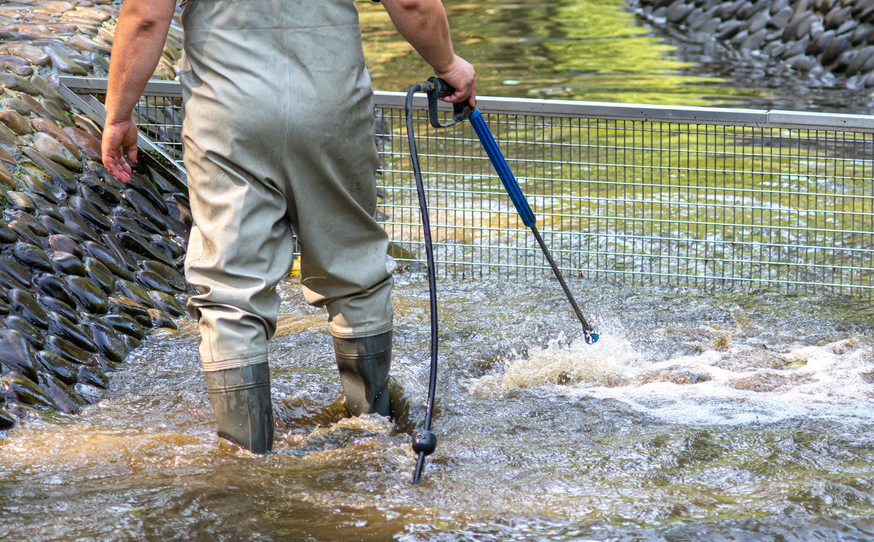 Pond cleaning process background. Man in high rubber boots cleans a garden pond with a high-pressure wash from sludge.