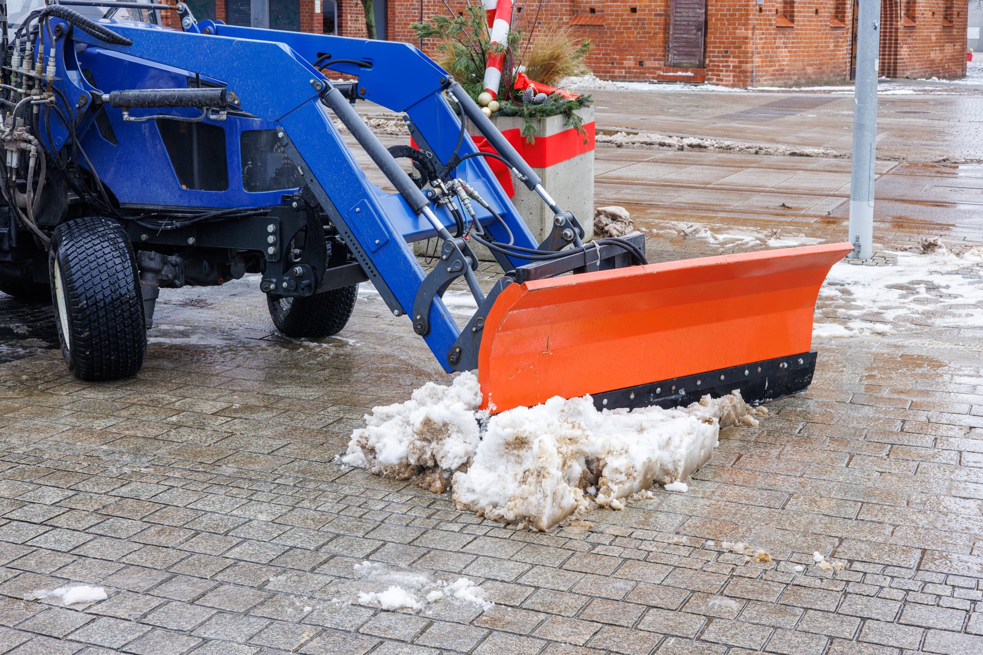 Front of a blue tractor with an orange bucket removing snow in a town square. High quality photo