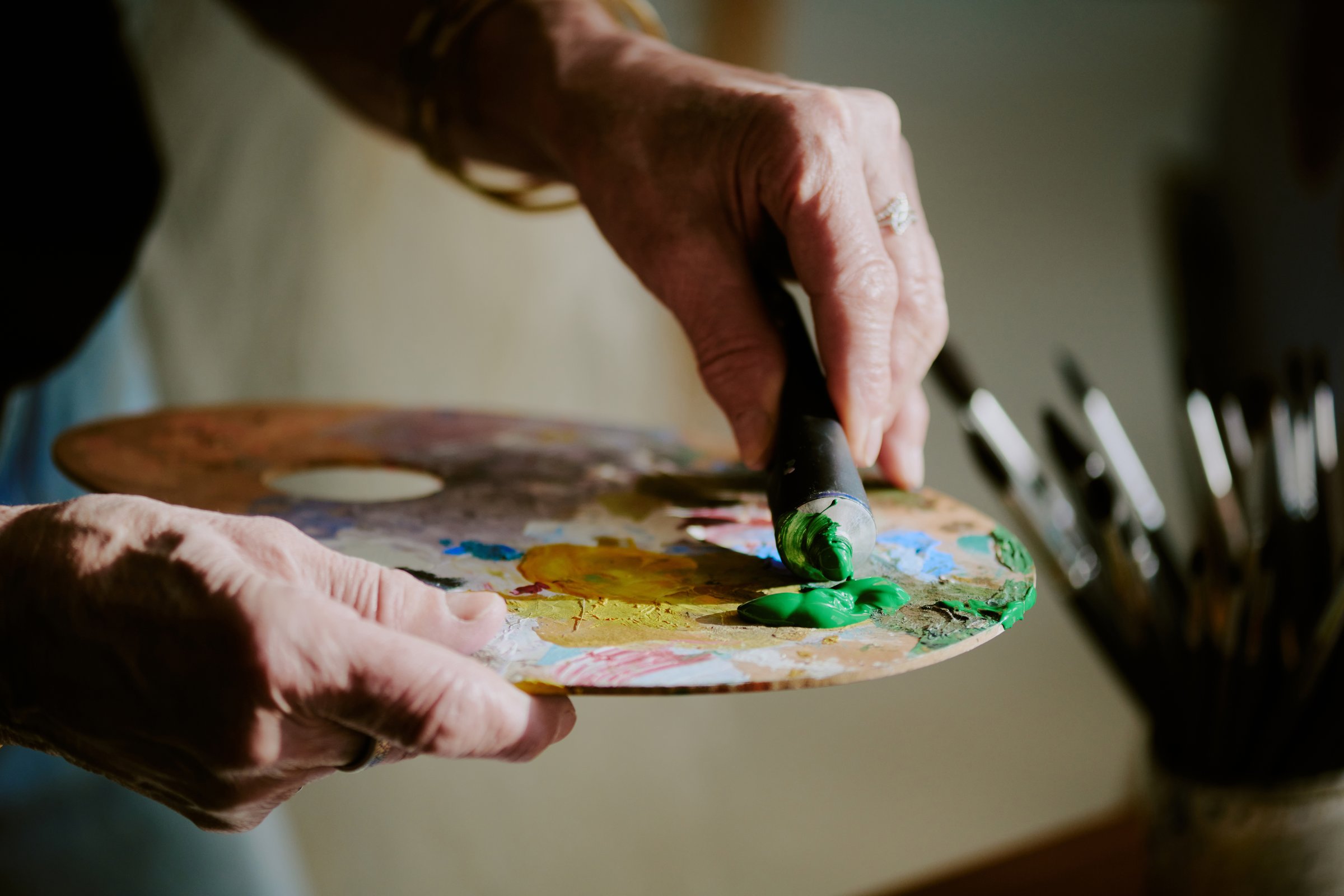 Closeup of hand of unrecognizable artist applying small amount of green oil paint from tube onto palette
