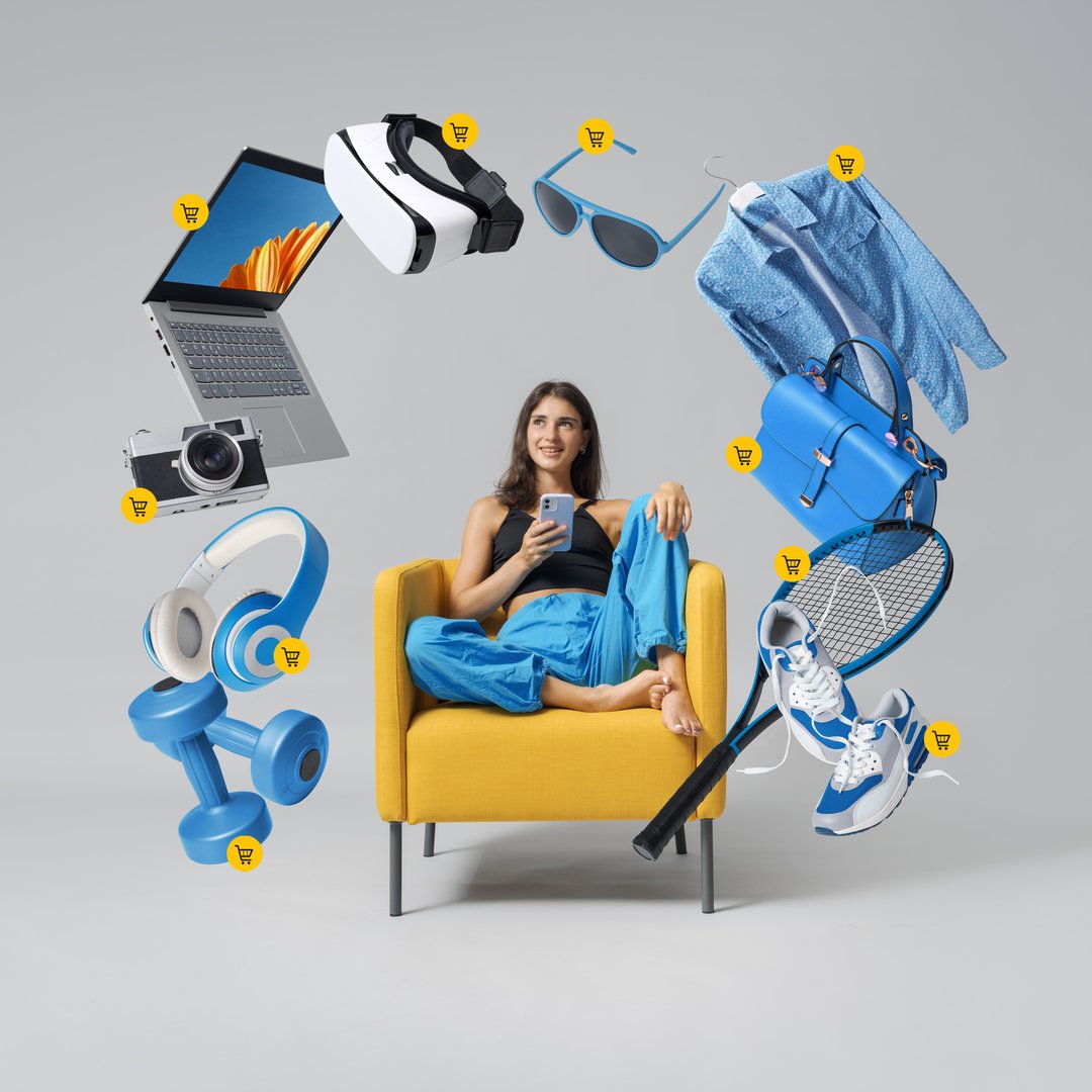 Happy teenage girl doing online shopping on her smartphone, she is surrounded by products on sale and she is adding them to her shopping cart