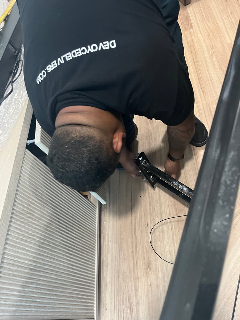 Person kneeling, assembling furniture with tools on a wooden floor.
