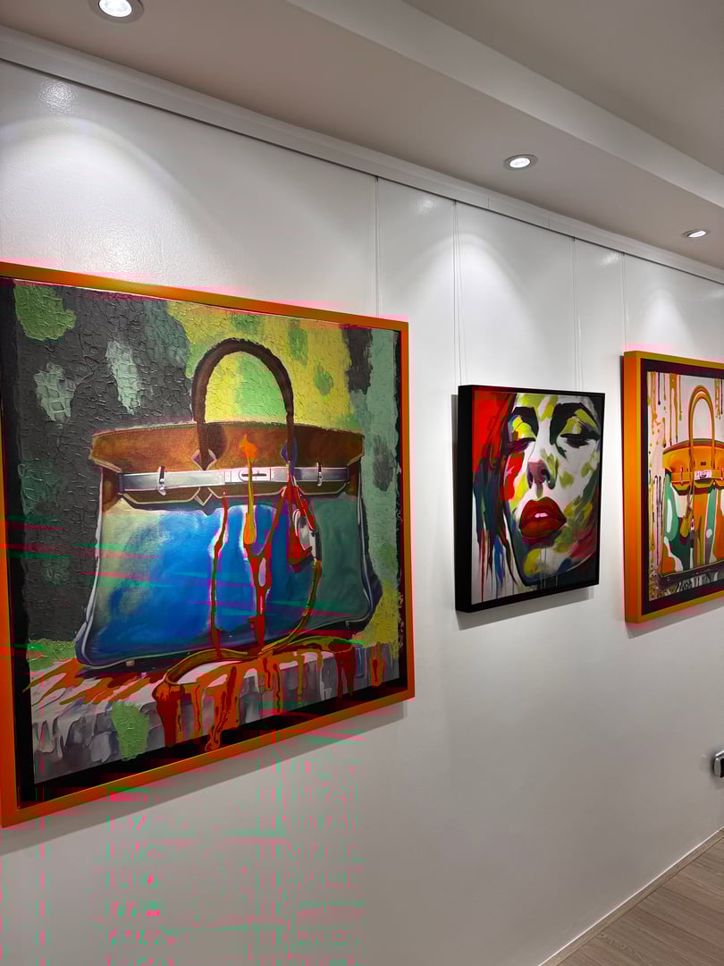 Gallery wall featuring colorful art, including a large handbag painting, a vibrant portrait, and another handbag.