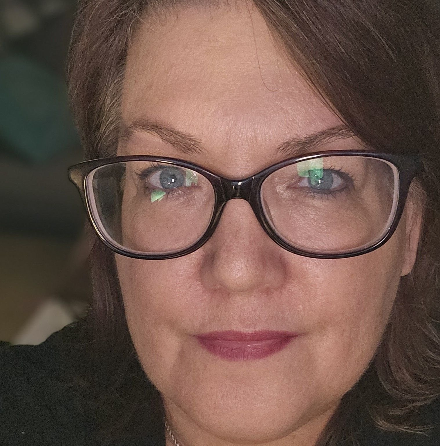 A person with glasses and brown hair, looking directly at the camera. The background is slightly blurred.