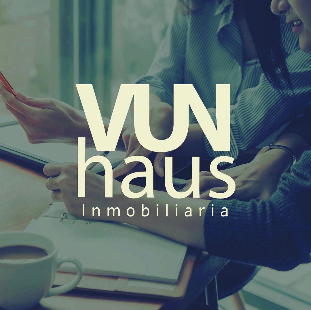 Two people reviewing documents at a table with a coffee cup, overlaid with text VUN haus Inmobiliaria.