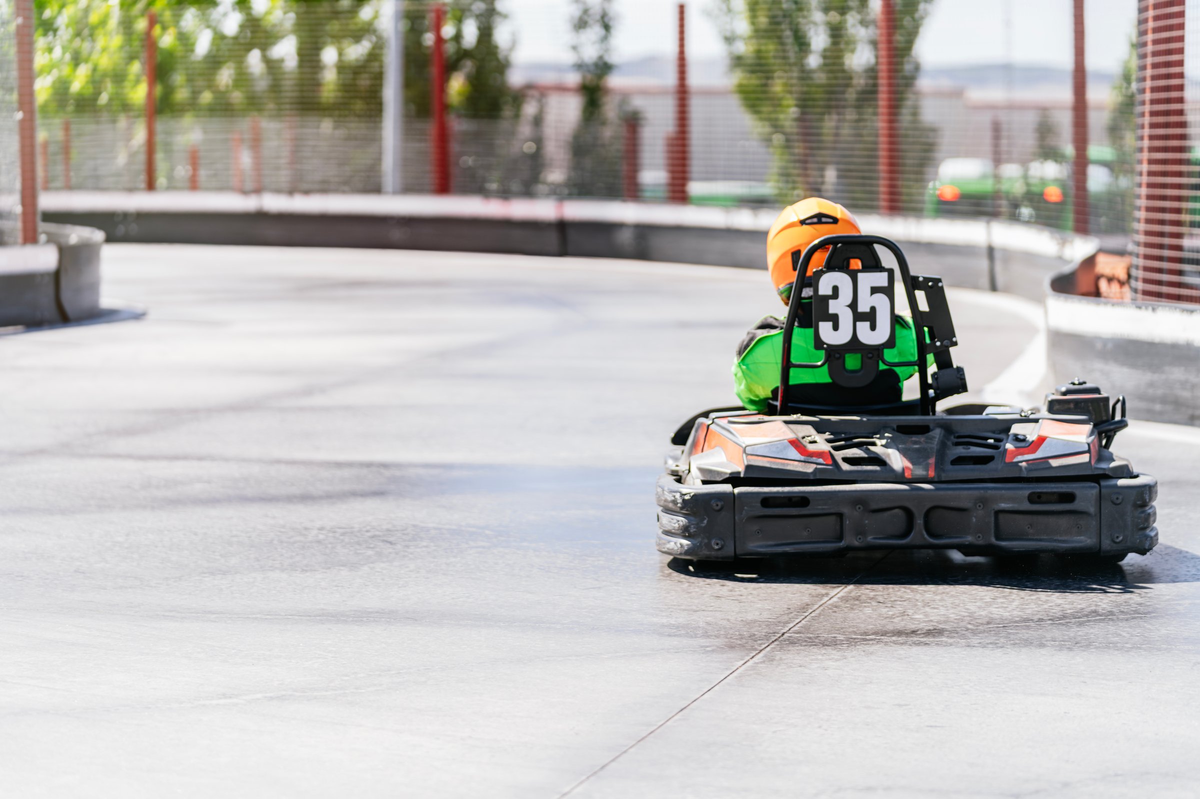 Child in an orange helmet and green racing suit driving a speedy go-kart with the number 35 on an outdoor track