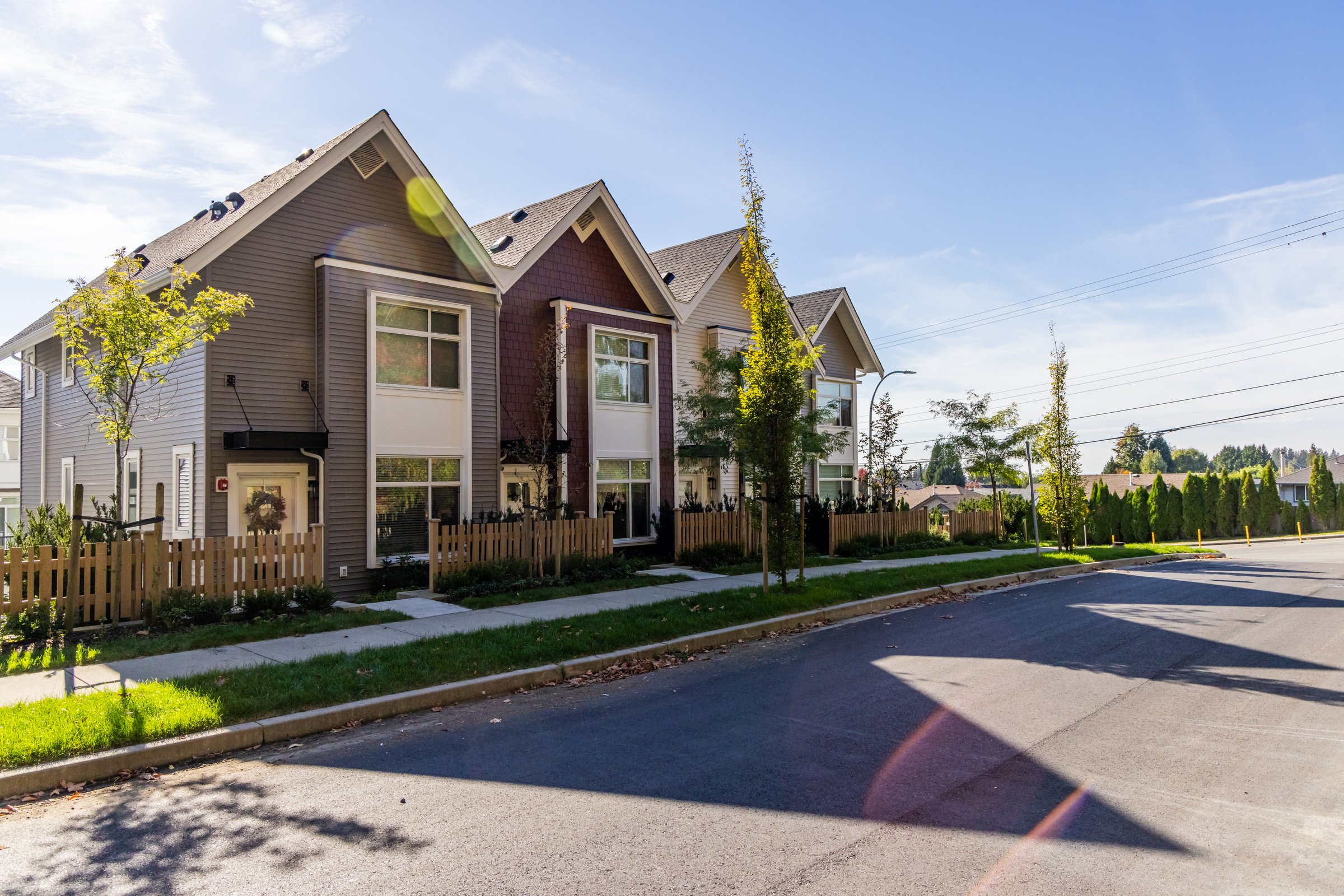 Row of modern townhouses with picket fences in Mission, BC, Canada, under a clear blue sky. The scene captures a tranquil suburban setting on a bright sunny day.