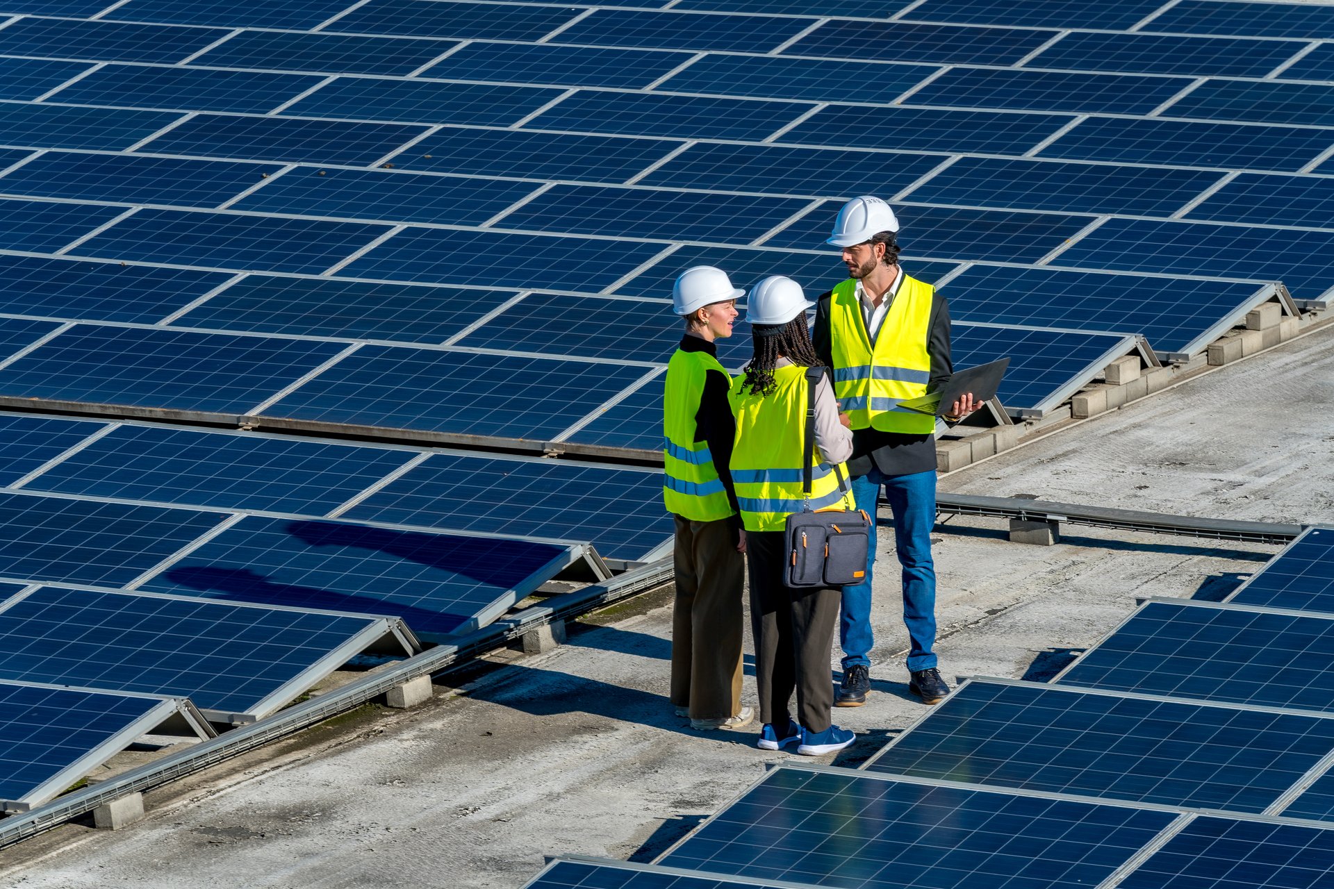 Three renewable energy engineers are inspecting and discussing solar panel installation on a commercial building rooftop, ensuring sustainable power generation and environmental responsibility