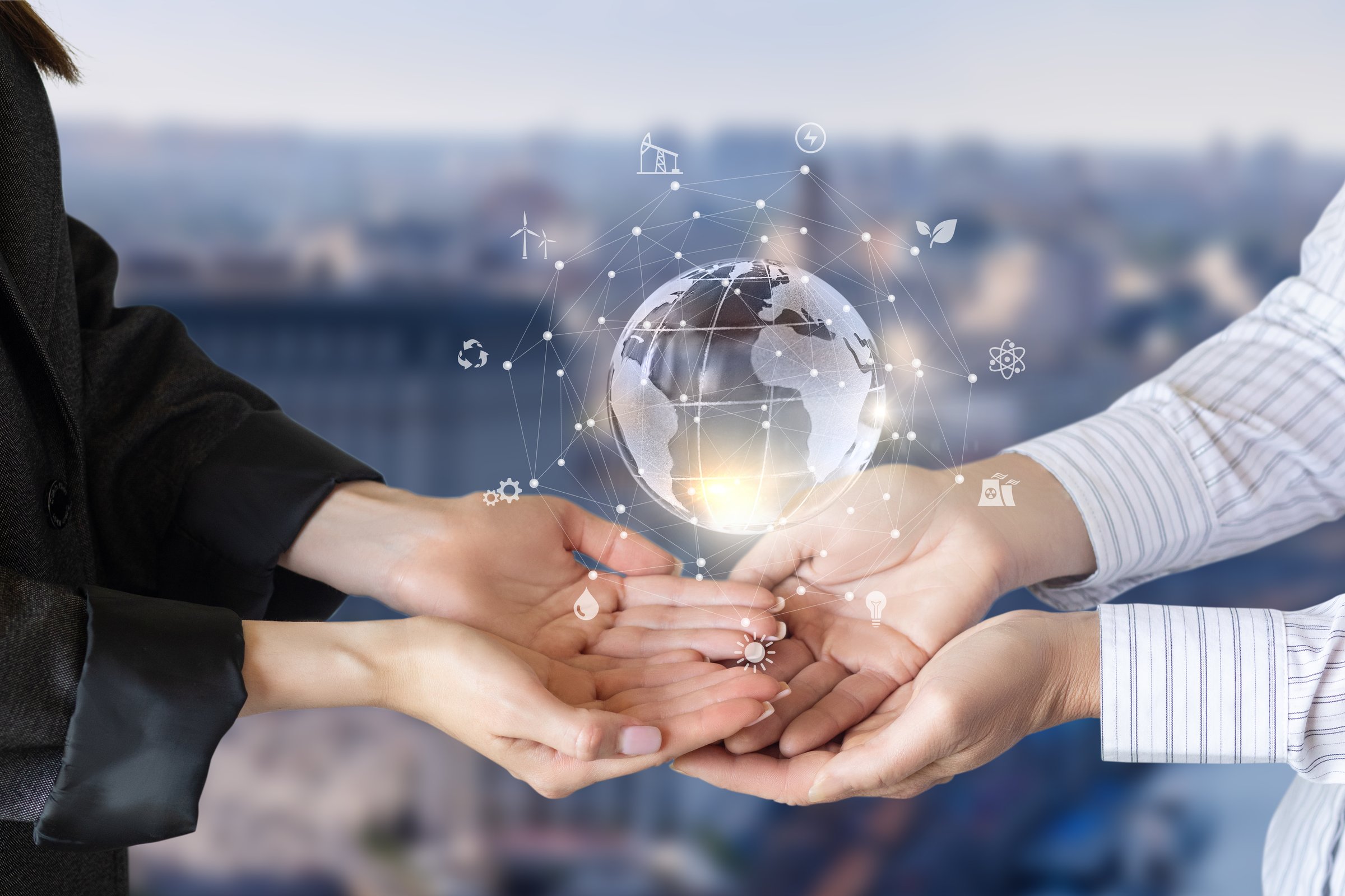 Two hands are positioned together to support a glowing globe, which features symbols of alternative energy, symbolizing global cooperation for sustainability in a modern urban environment.