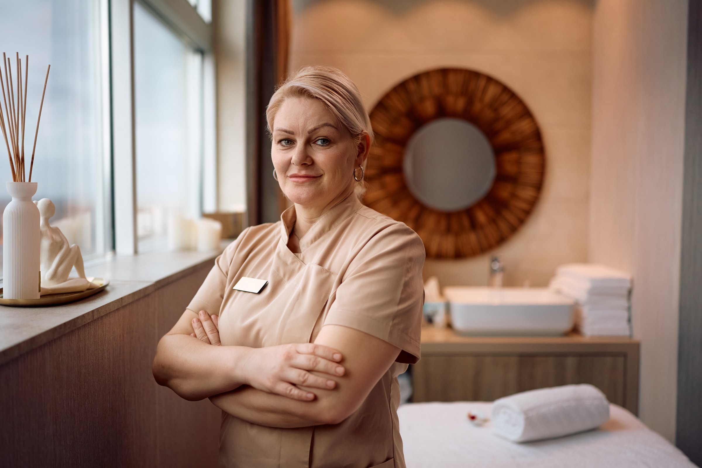Massage therapist standing with her arms crossed at health spa and looking at camera.