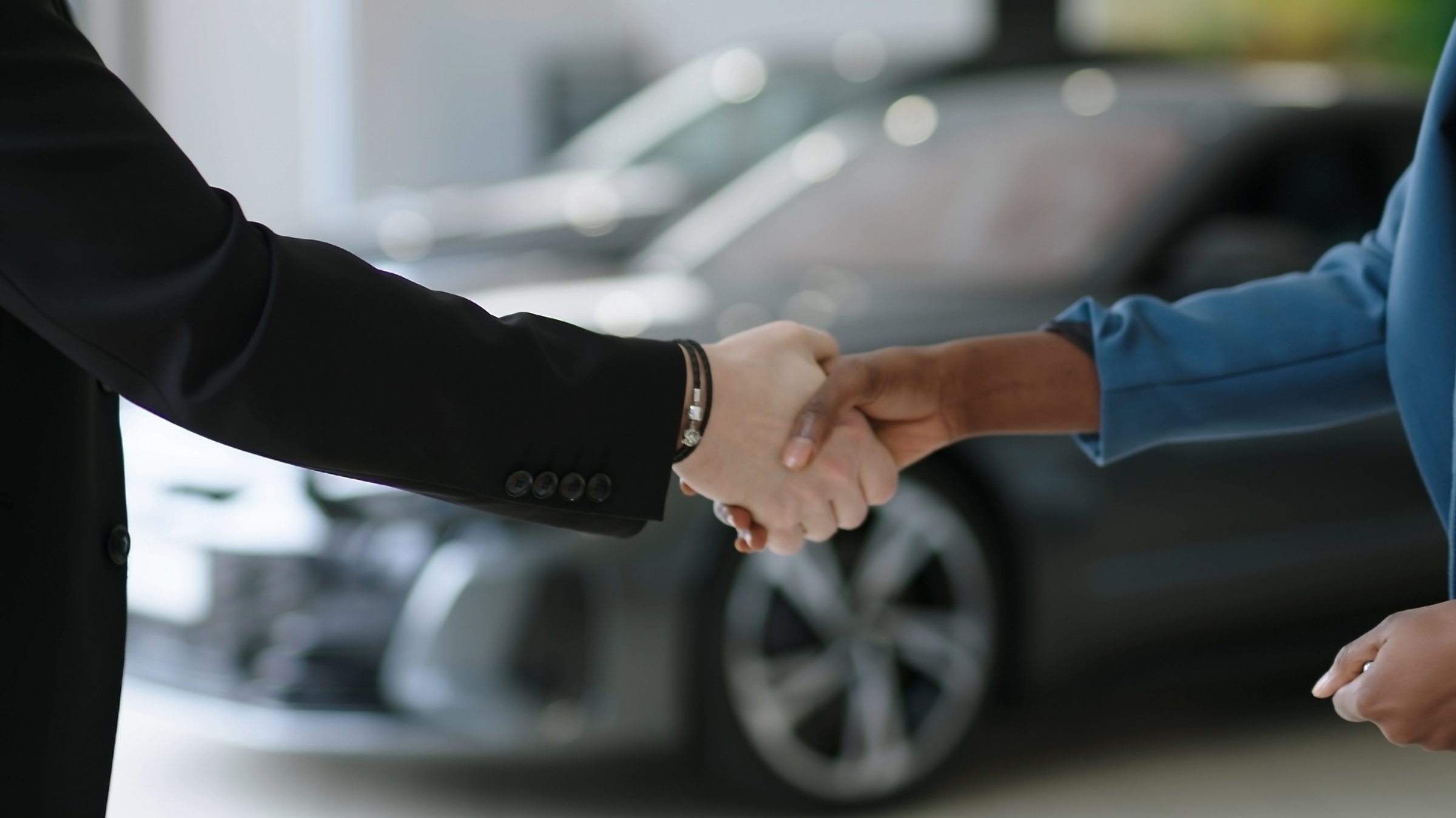 Cropped close-up of a car dealer shaking hands with his client - African woman buying a car.