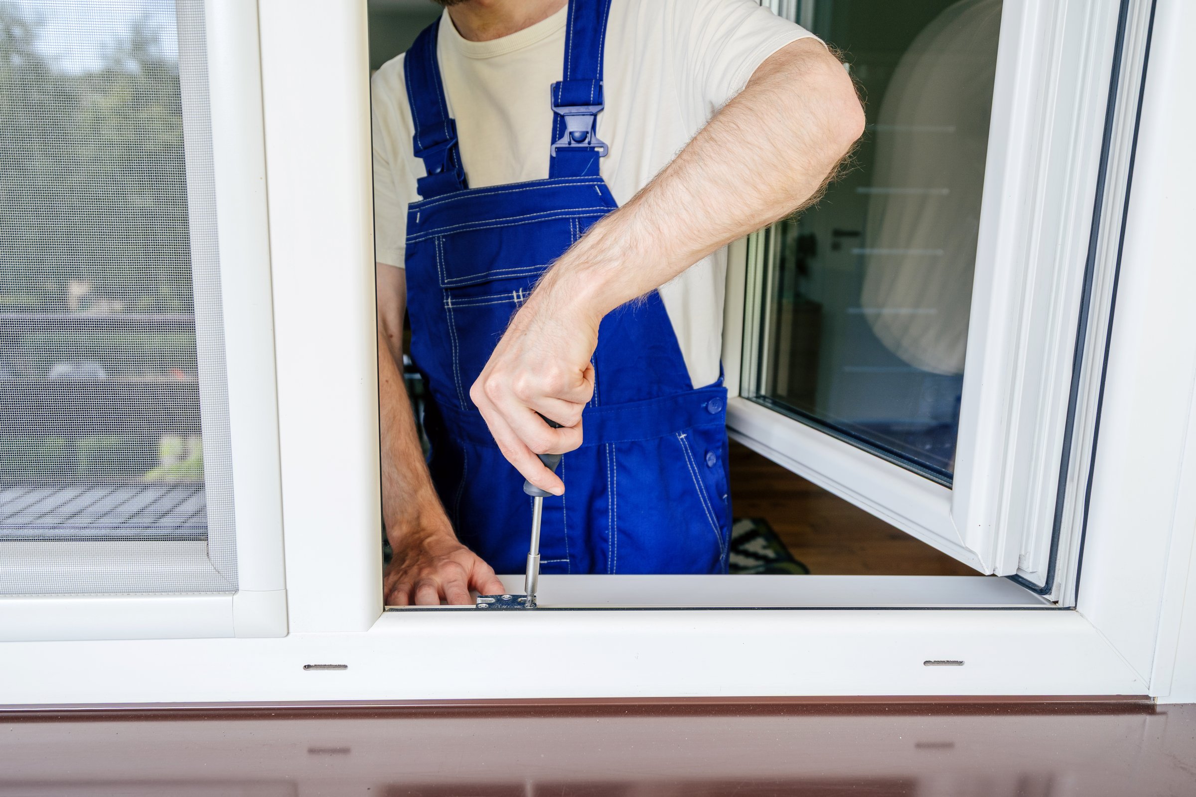 Cropped shot of a repairman installing new double glazed PVC window frame at residential building, using screwdriver tool. The focus is on ensuring comfort and durability for the home interior design
