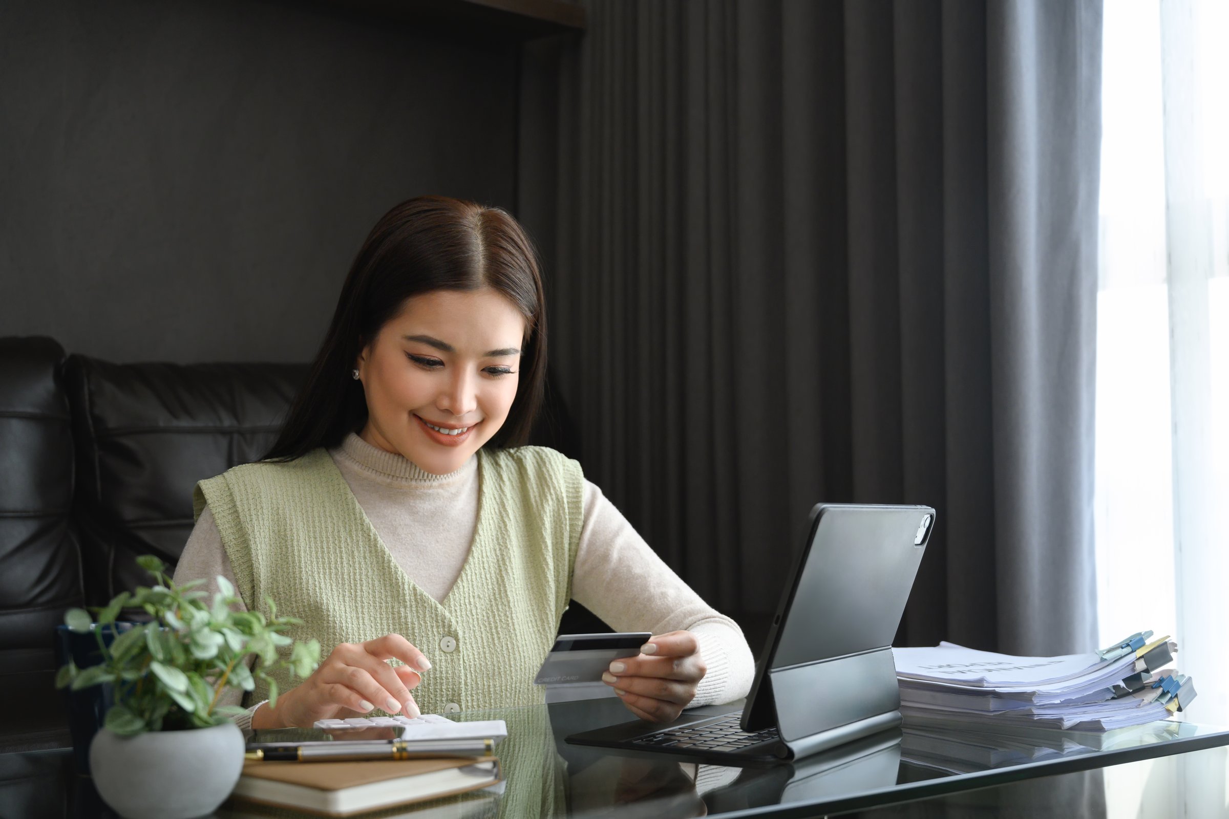 Attractive young woman holding credit card and calculating monthly expenses at home.