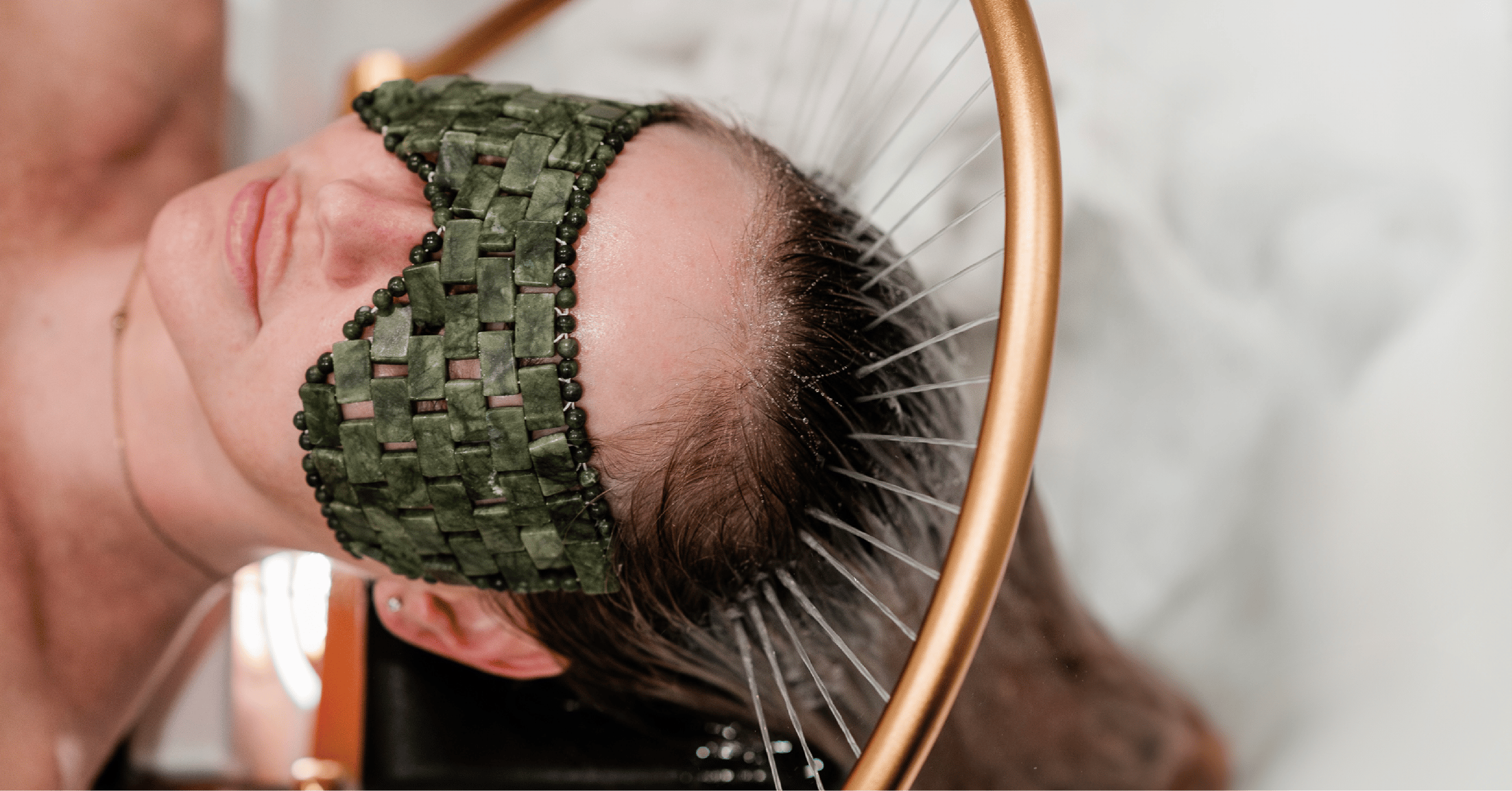 Person lying down with an eye mask and a circular metal structure around their head, resembling a relaxation spa setting.