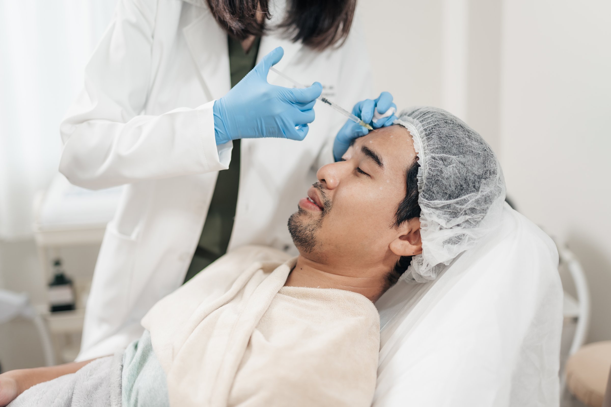 Asian man getting rejuvenation injection on his forehead by face care specialist. Anti aging on face.